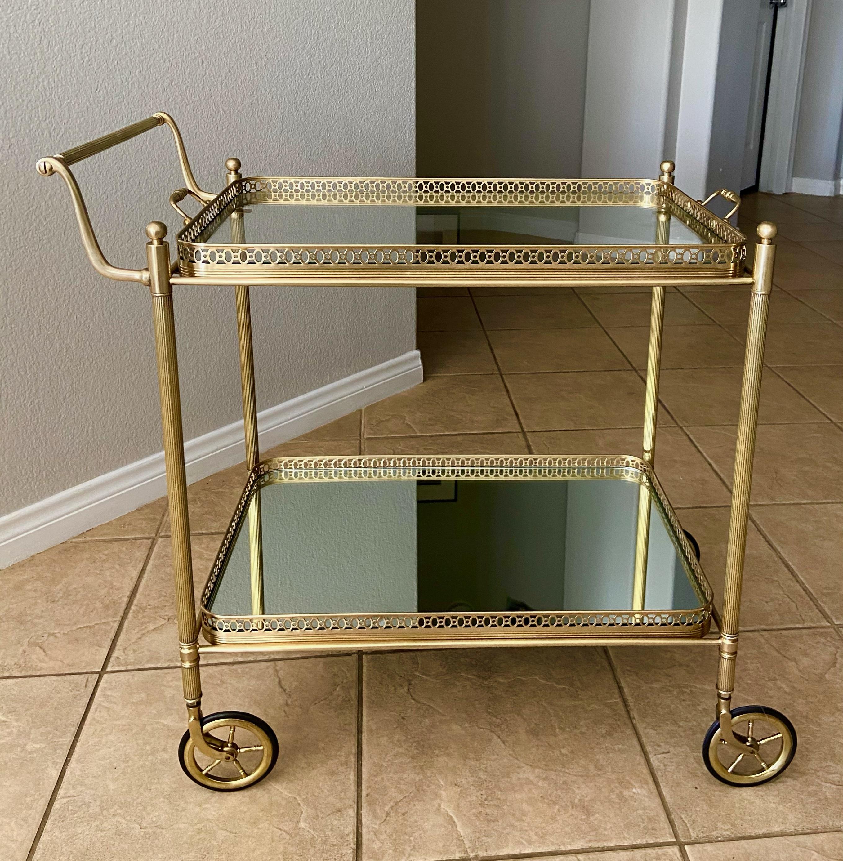 French brass bar cart with two-tier glass inset shelves, bottom shelf has mirrored glass, the top shelf has clear glass. Great detailing including reeded legs, pierced trays and solid brass casters. Top self can be removed and used a service tray