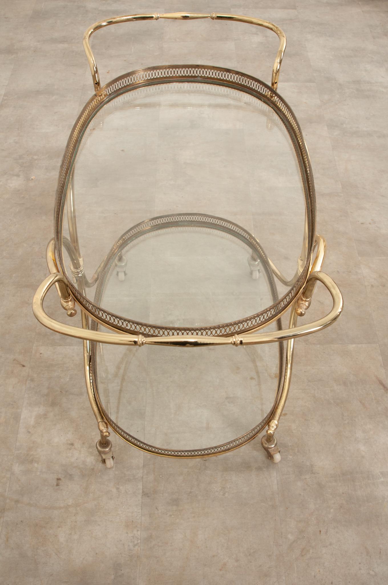 An elegant brass bar cart or trolley is the perfect occasional table for your interior. This curvy tiered bar cart features two oval glass surfaces surrounded with pierced galleries, both are removable. The handles are accessorized with a knotted