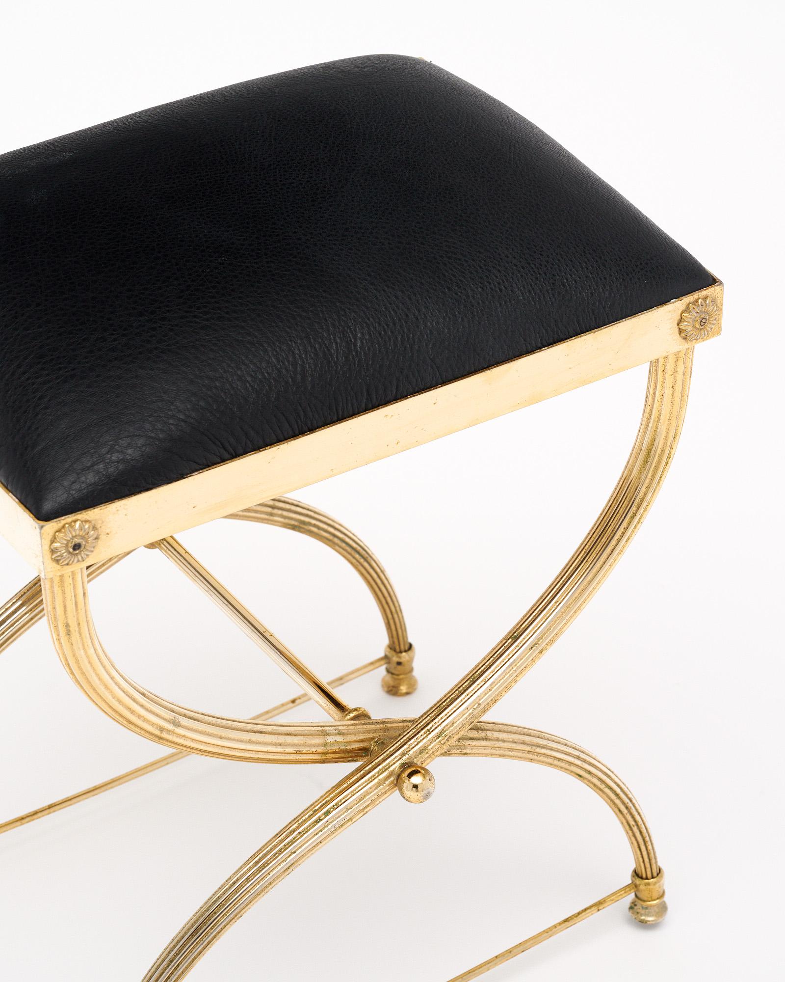 Tabouret français en laiton massif doré. La structure présente de magnifiques pieds curule striés avec des brancards. Le siège a été recouvert de cuir noir. Cette pièce est en très bon état et ne présente qu'une usure superficielle mineure due à