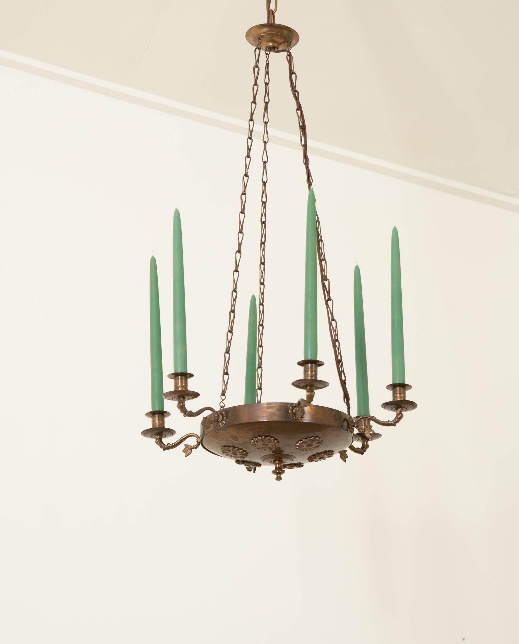 A lovely hand-crafted brass six arm chandelier made in 20th century France is just as pretty as it is functional. The wonderfully patinated brass bowl is decorated with rosettes and has an elegant finial in its center. Inside you will find it is