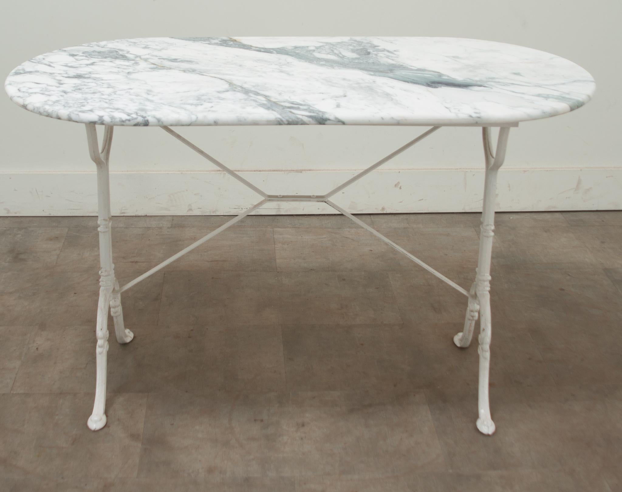 A classically styled French bistro table featuring a white capsule-shaped marble top over a painted cast iron base. This petite dining table shows wear consistent with age and use. Be sure to view the detailed images to see the current condition.