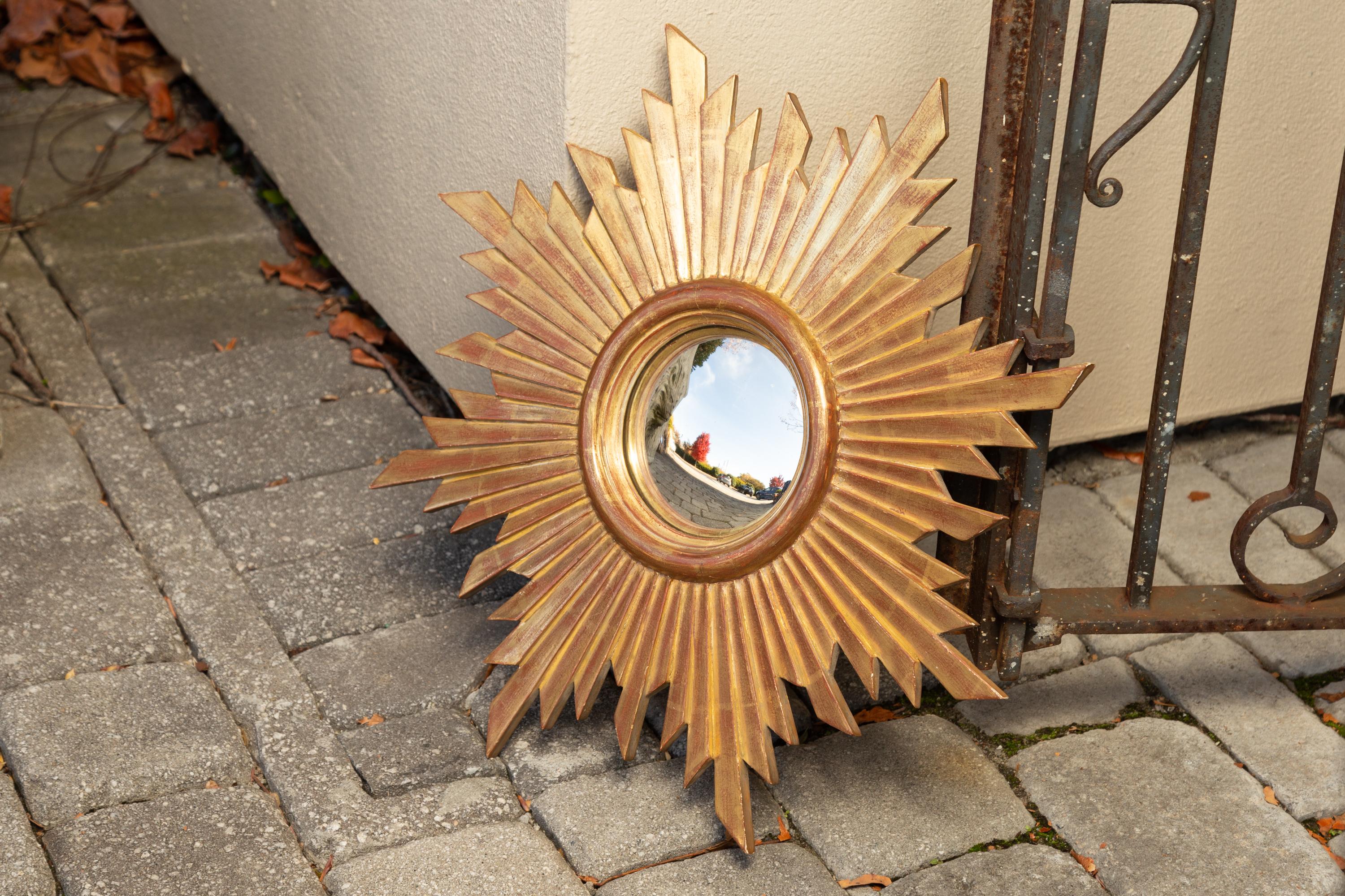 A vintage French giltwood sunburst with convex mirror plate from the mid-20th century. Born in France during the midcentury period, this giltwood sunburst features a central convex mirror plate, surrounded by a molded inner frame with subtle red