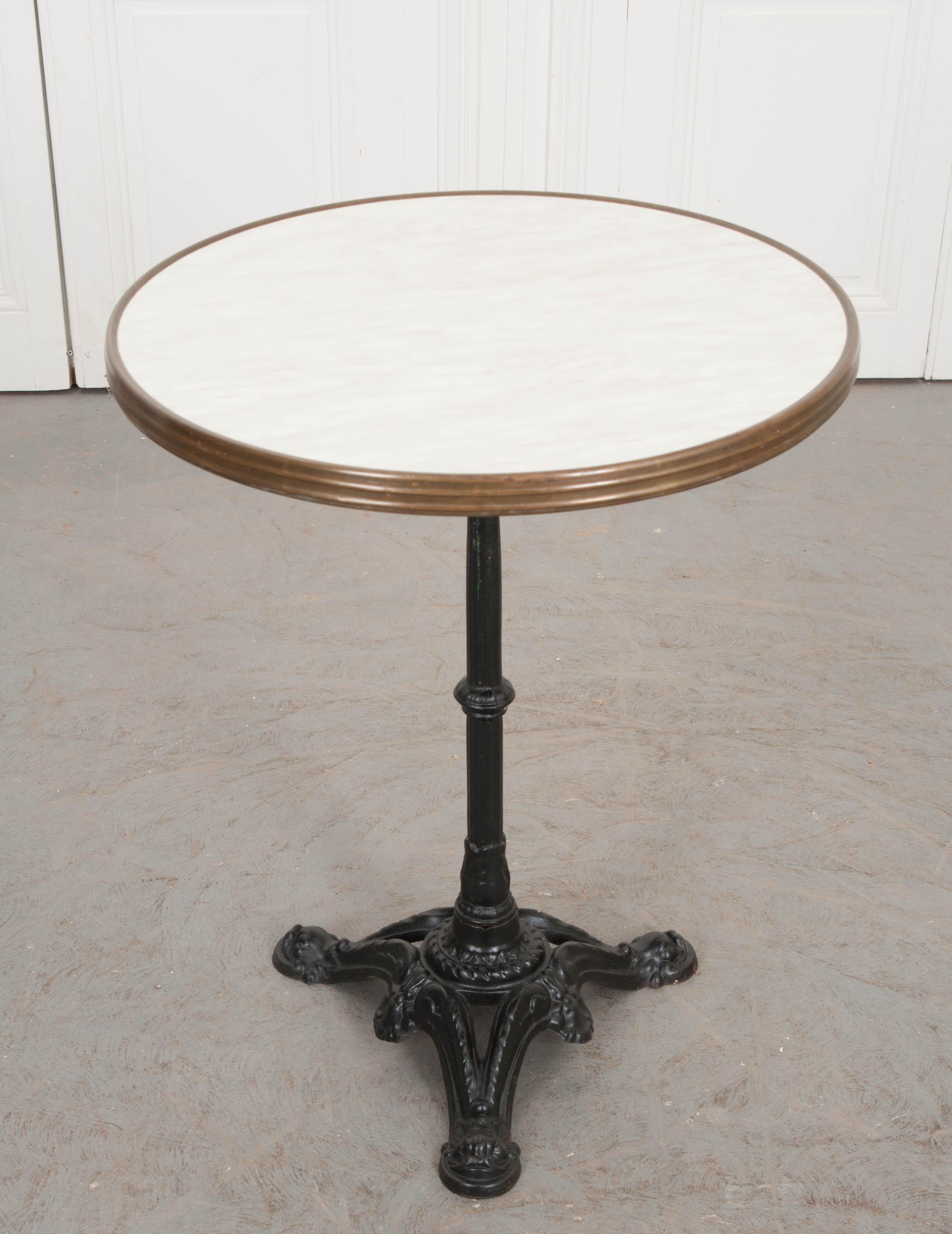 Picture yourself reading a novel at this charming vintage cast iron bistro table, circa 1950, on a Champs Elysees sidewalk in Paris! It features a white cultured-marble top with grey veining that is banded in brass and resting on a black-painted