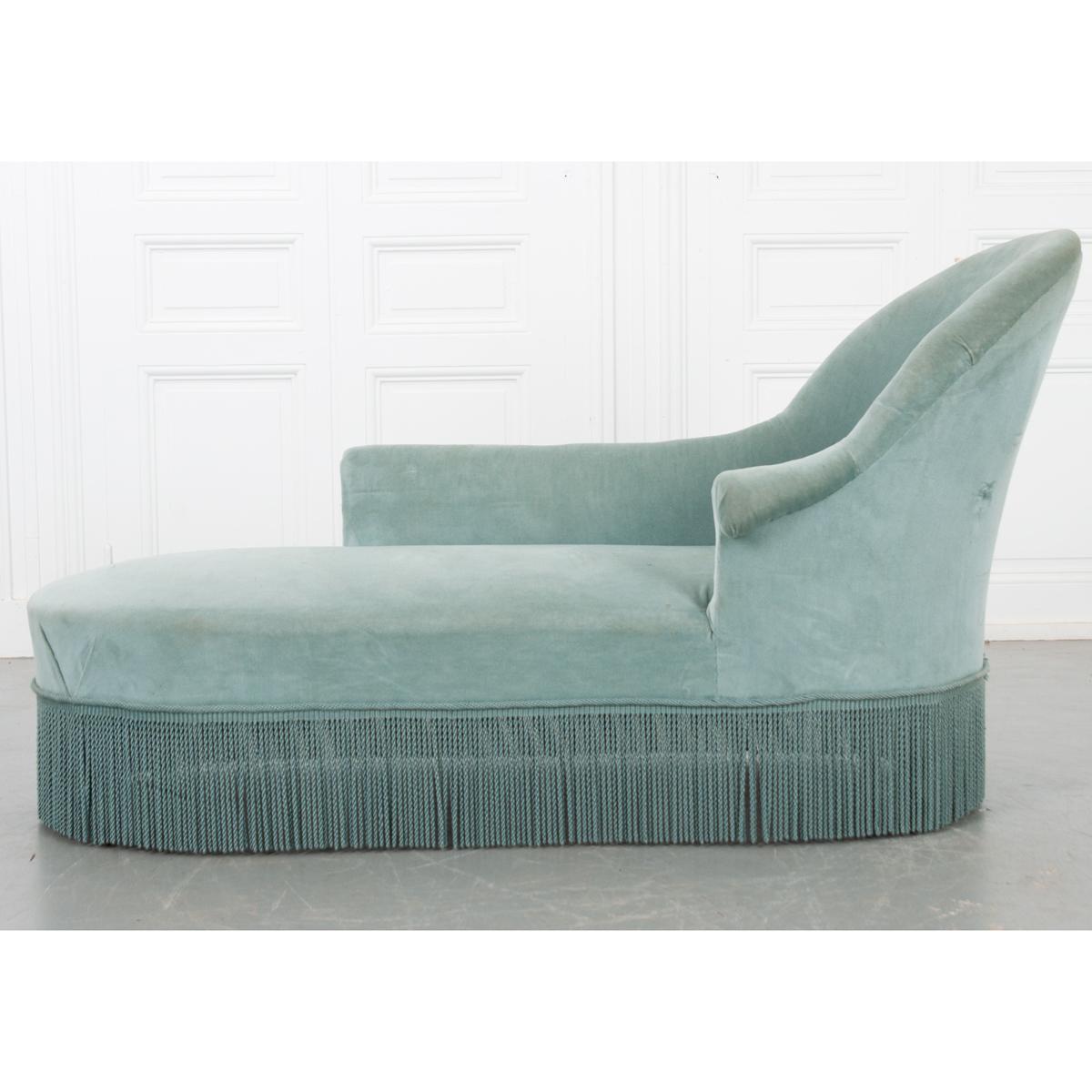 A beautiful light blue velvet chaise with a classic shape and fringe around the bottom to hide the turned wooden feet. The perfect combination of comfort and composition, this chaise would go perfectly in any living space. The upholstery is slightly