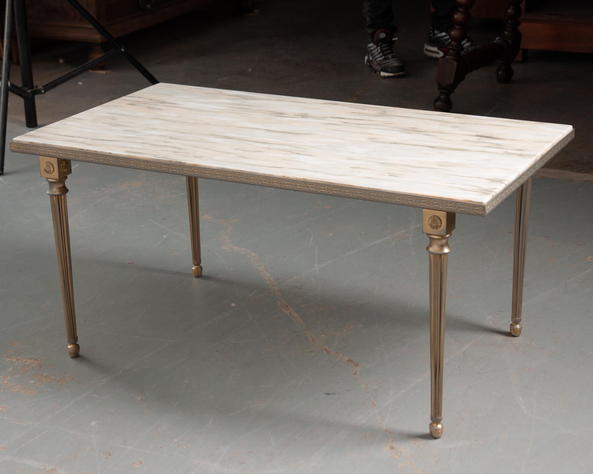 A stunning vintage coffee table crafted in France. The inset marble top is in good condition and features unique veining. The sleek mixed metal base in the style of Louis XVI highlights the intricate scrolling details that borders the top. A square