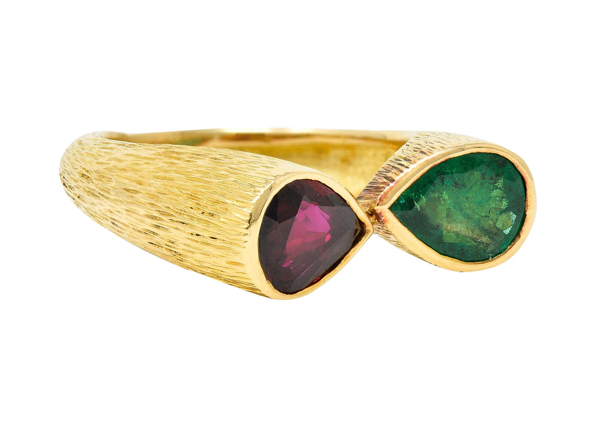 Highly textured ring features two pear cut gemstones - bezel set and mirroring one another

Emerald is vibrantly green and semi-transparent with natural inclusions while weighing 0.84 carat

Ruby is strikingly transparent with medium dark red color