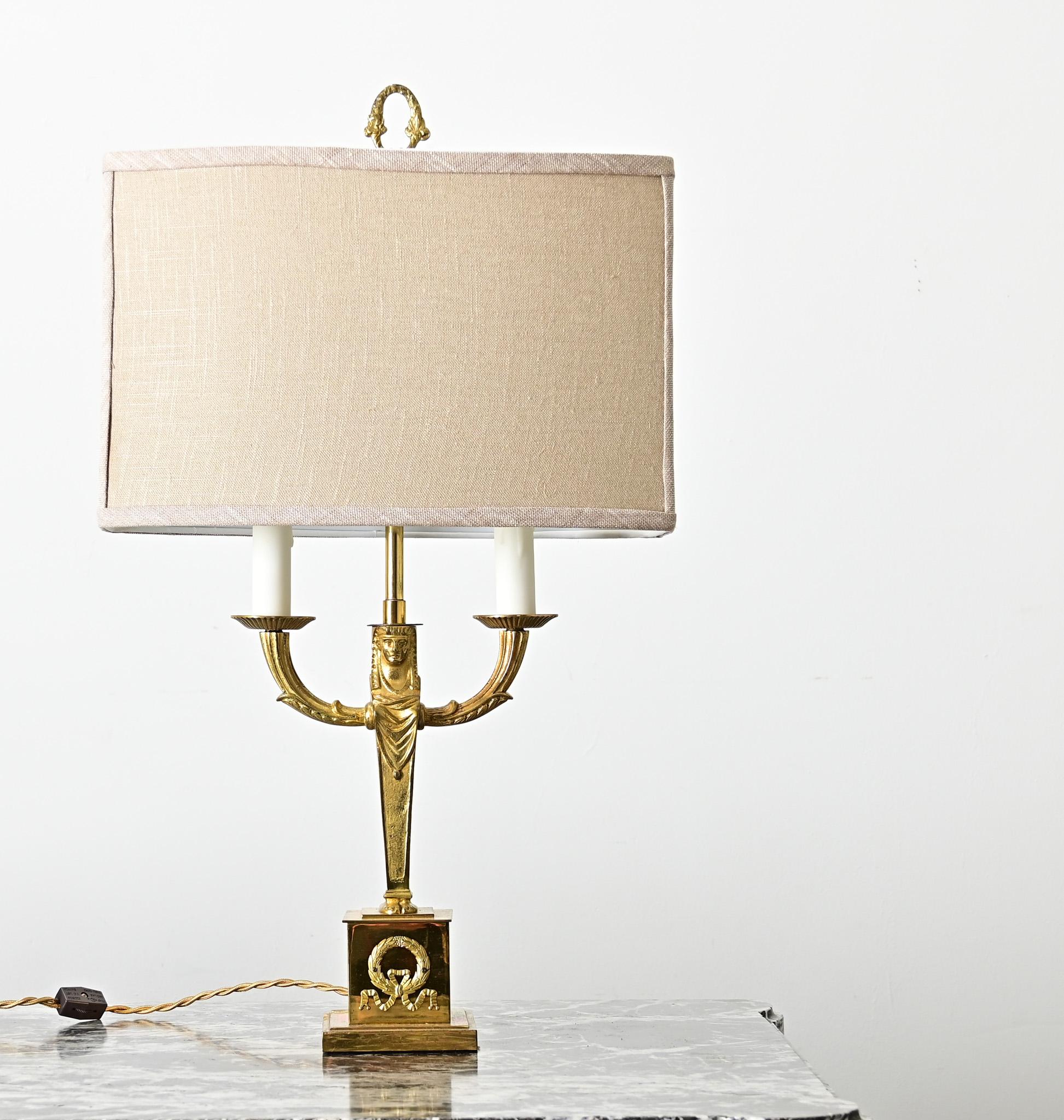 French vintage (early 20th century) Empire style cast brass table lamp with custom linen shade. This striking fixture contains a multitude of references across the Mediterranean world: a stylized female figure for a base dressed like a royal of