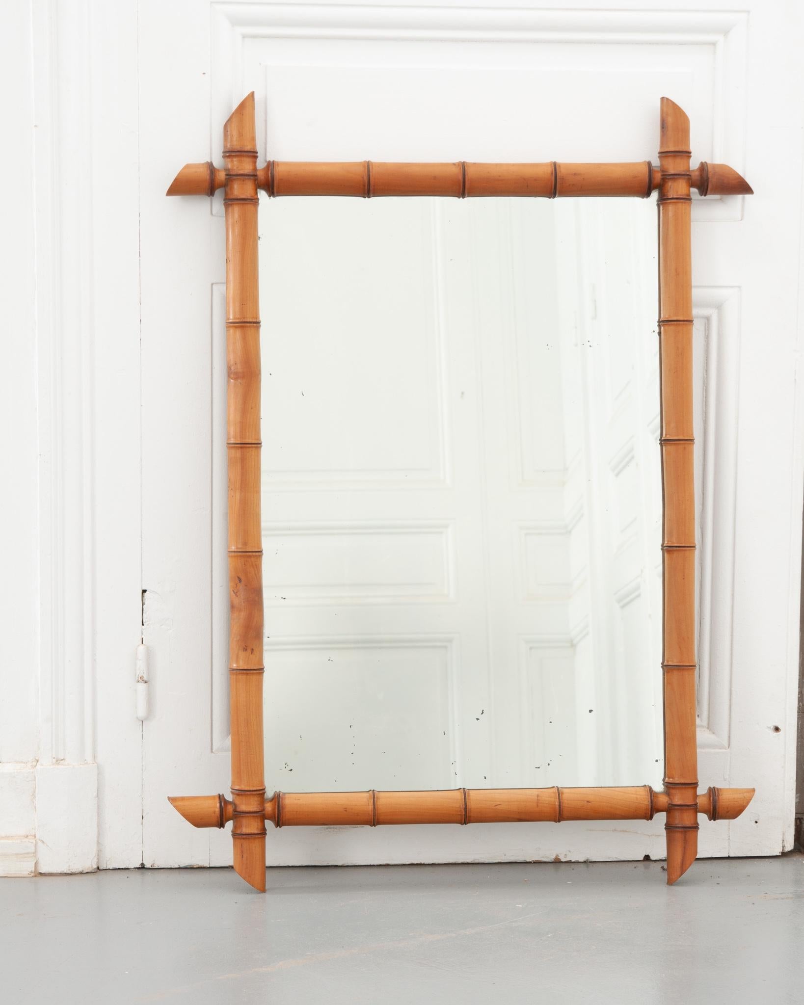 A French vintage rectangular faux-bamboo mirror from the 20th century, with a lovely honey brown patina. This rustic mirror features a rectangular silhouette made of a carved faux bamboo frame showcasing intersecting corners. Already fixed with a