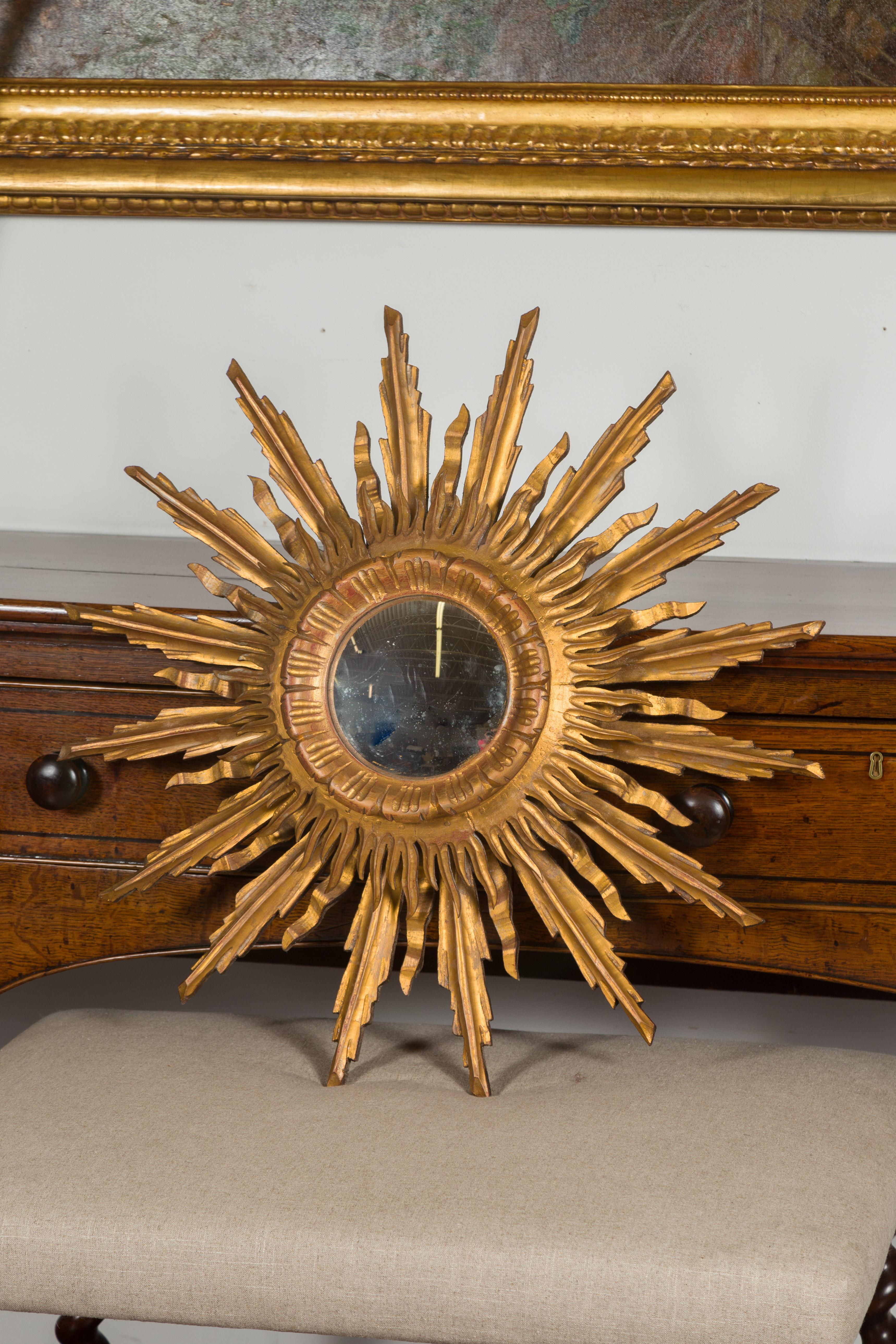 A French vintage giltwood sunburst convex mirror from the mid-20th century, with rays of varying heights. Created in France during the midcentury period, this sunburst mirror charms us with its graceful lines and golden finish. Surrounding a central
