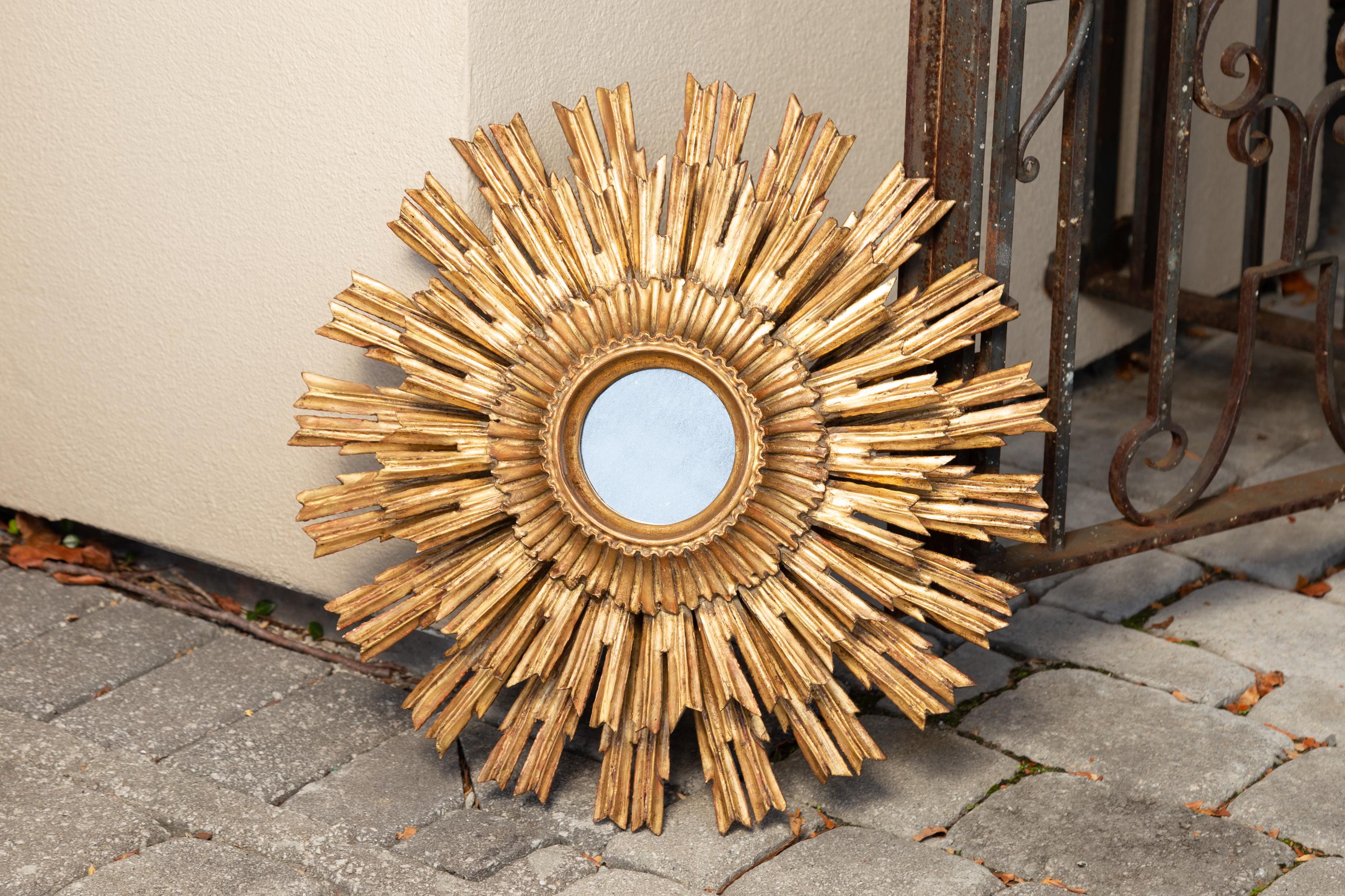 A vintage French giltwood sunburst mirror from the mid-20th century, with layered rays and small mirror plate. Born in France during the mid-century period, this exquisite sunburst mirror features a petite central mirror plate surrounded by a molded