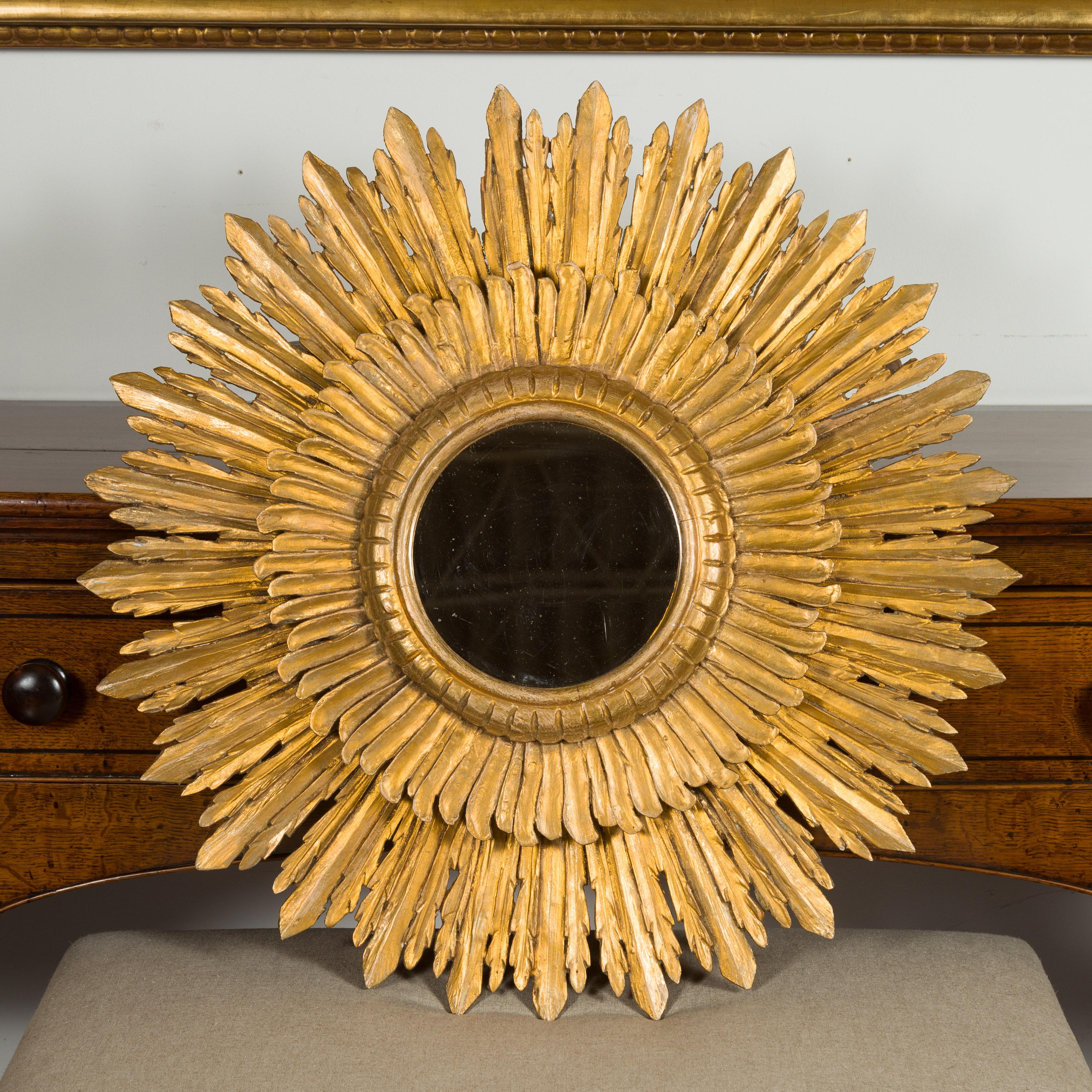 A vintage French giltwood sunburst mirror from the mid-20th century, with layered rays and small mirror plate. Created in France during the midcentury period, this sunburst mirror features a central mirror plate surrounded by a molded frame resting