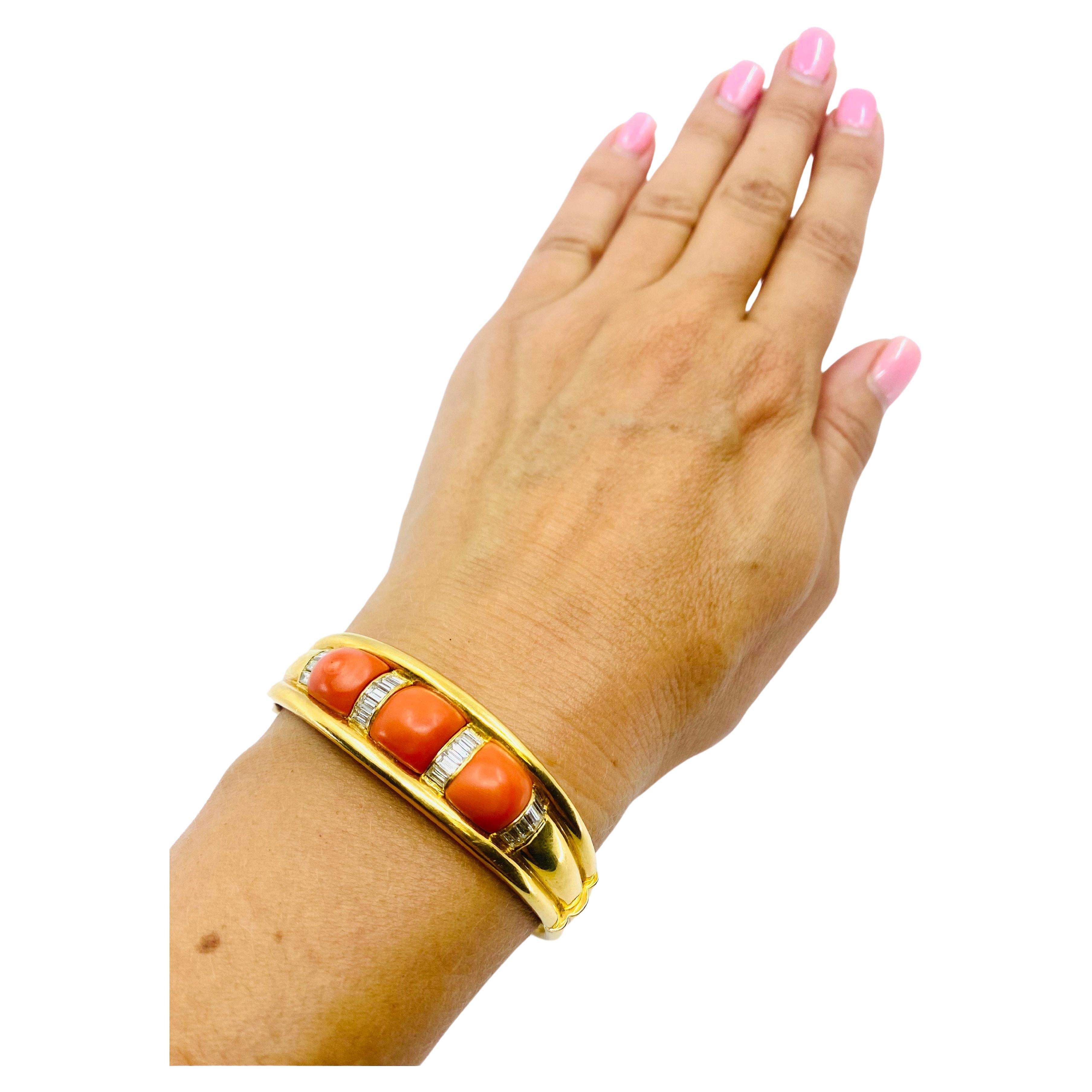 A vintage 18k gold bangle bracelet features coral and diamond. There are three cabochon cut corals arranged between four vertical diamond lines. The diamonds are baguette cut, beautifully staged by invisible setting. The bangle is fluted which