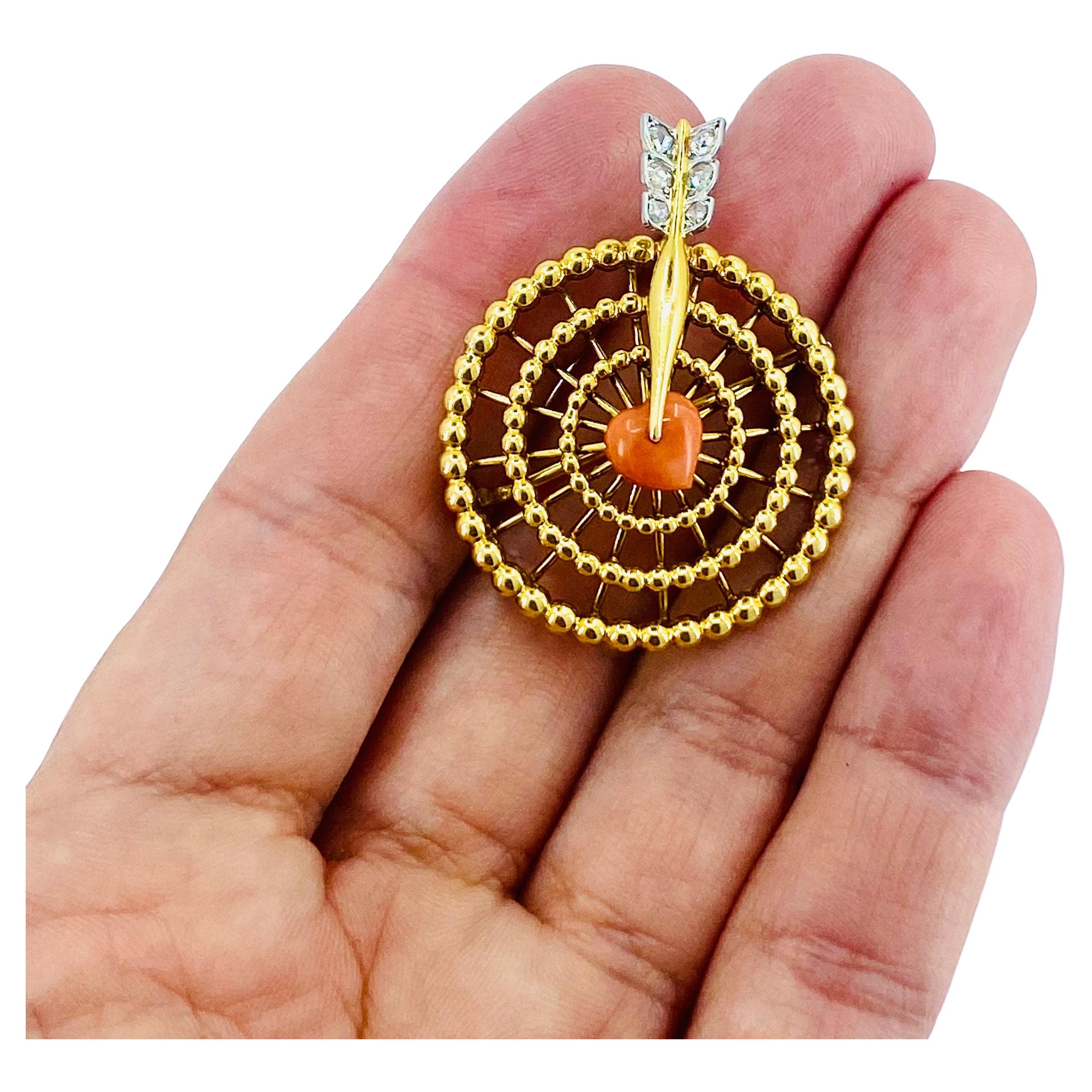 A lovely French vintage 18k gold brooch that features coral and diamonds.  It looks like a stylized dartboard with an arrow piercing a coral heart.The open-work dartboard is made of tiny gold balls arranged in circular patterns. The heart with the