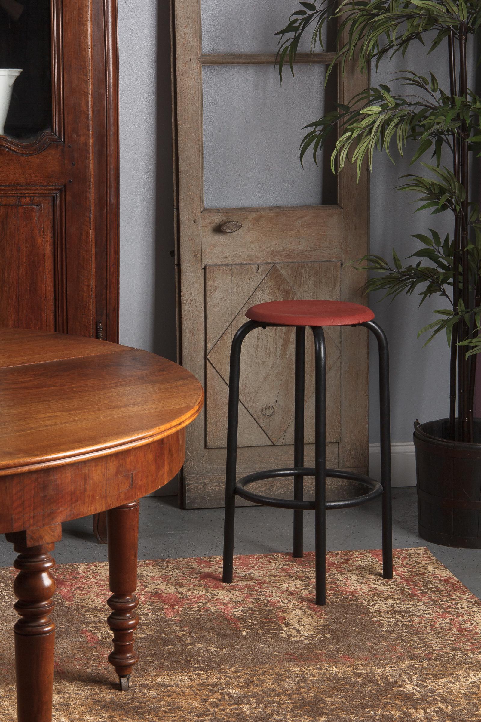 A midcentury French Industrial stool with tubular metal legs painted black and a round pine seat painted red. The seat is 12.5