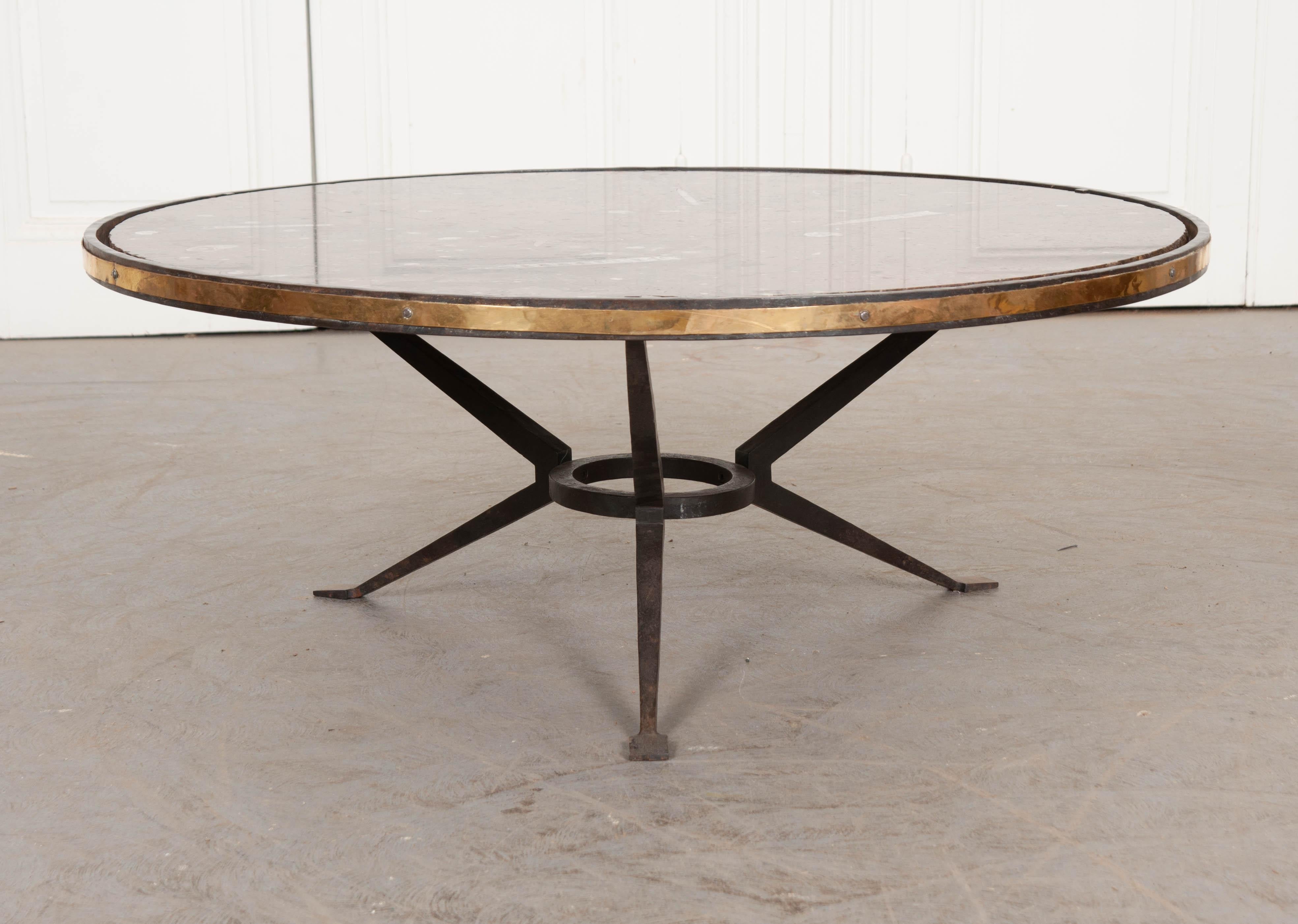 This refined coffee table was made in France, circa 1950. This unique table is a true one-of-a-kind. The table’s base was forged by hand out of iron. The circular piece of fossil marble that tops the table is spectacular and features a hand-chiseled