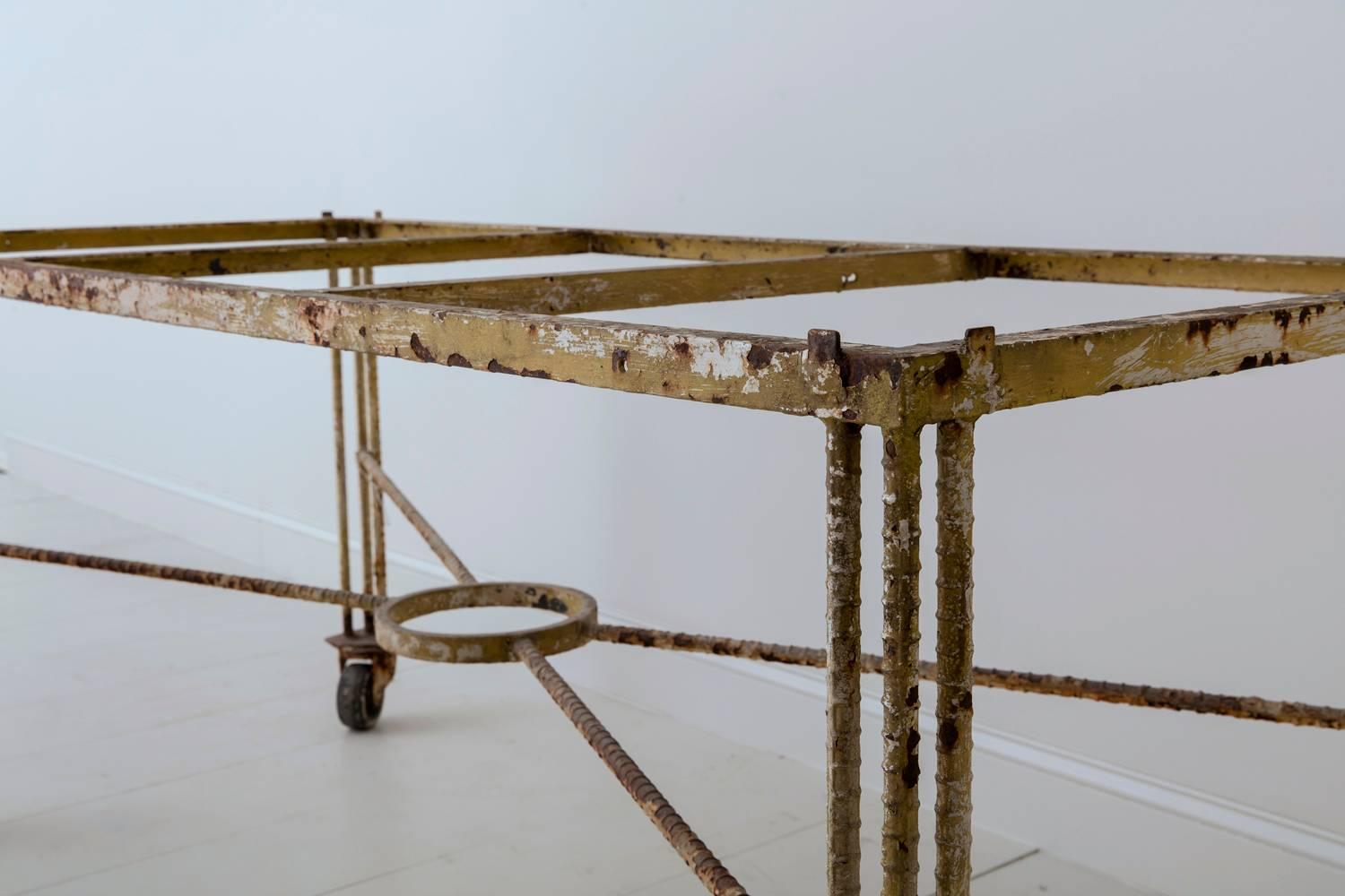 An early 20th century French industrial table base constructed with rebar legs and iron frame. This piece features a cross support and the legs sit on caster wheels. The original paint is a pale yellowish taupe wearing to reveal gently rusting