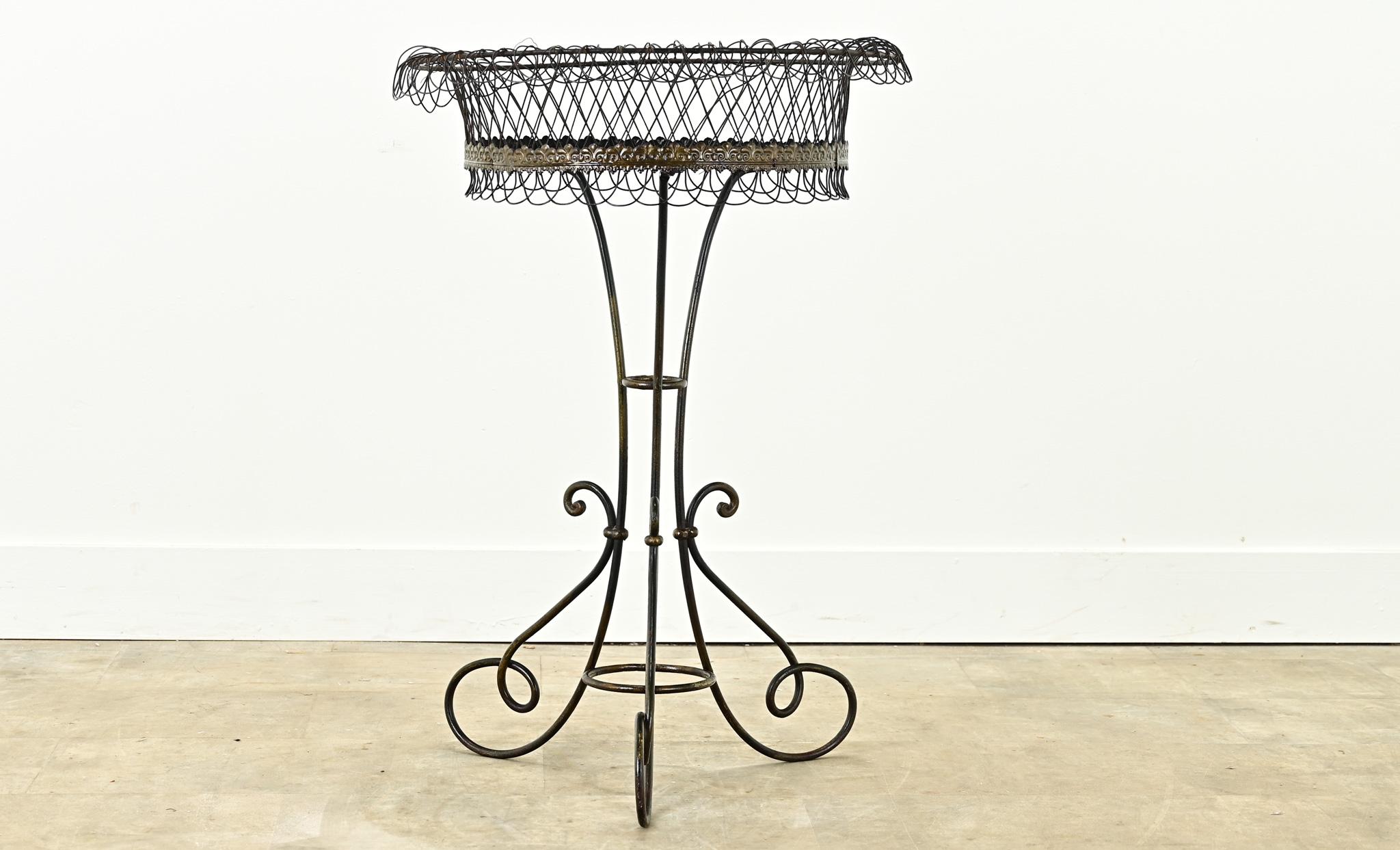 A vintage iron plant stand made in France. This round plant stand has a wrought iron wired basket and base ending on three scroll legs. Be sure to view the detailed images to see the current condition. 