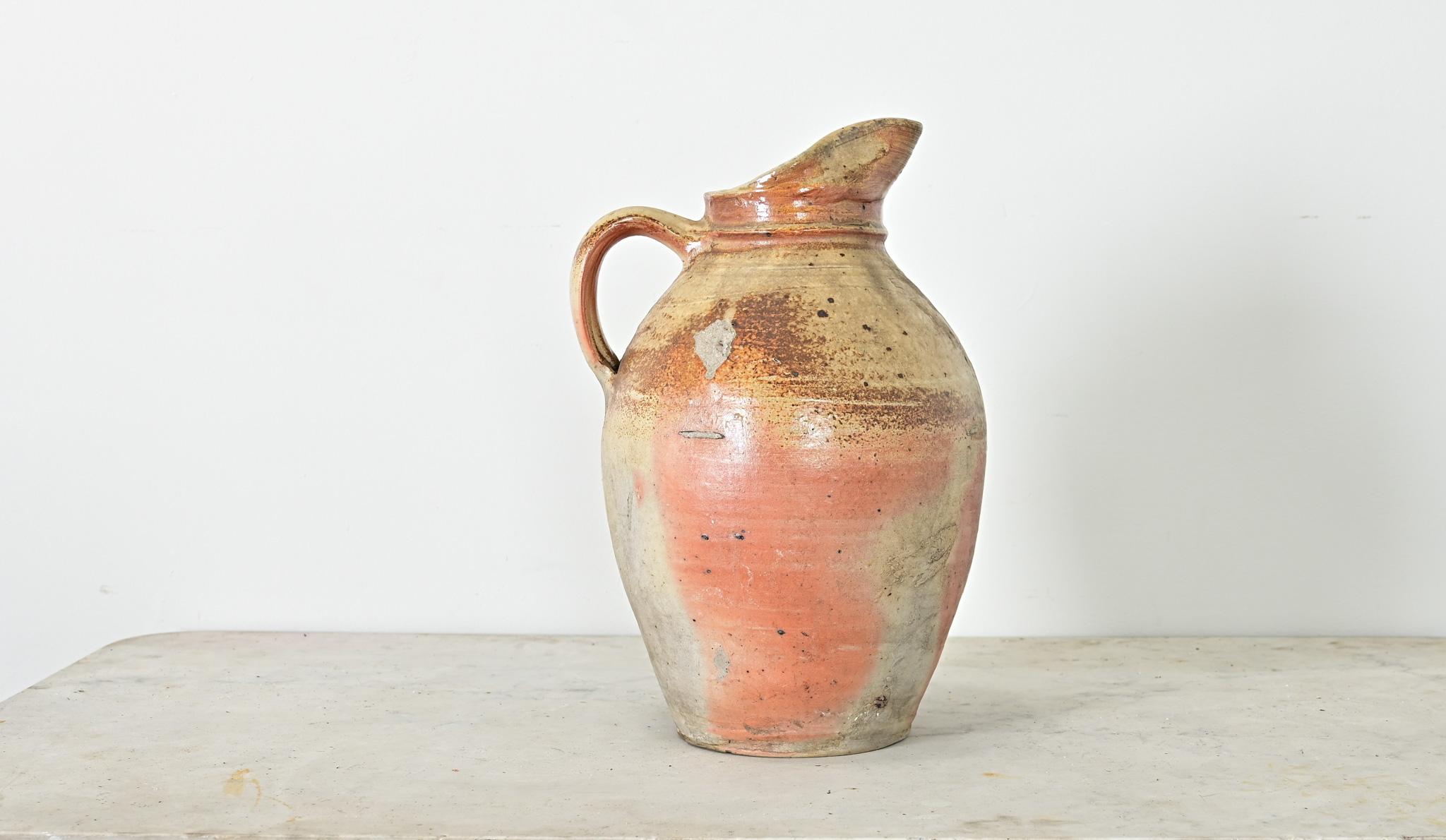 A French vintage glazed stoneware pitcher of unprecedented scale, this utilitarian Provincial vessel would have been used to dispense cider, wine, or water. Glazed in a ruddy blend of earthtones over the ribbed body, it becomes a unique work of