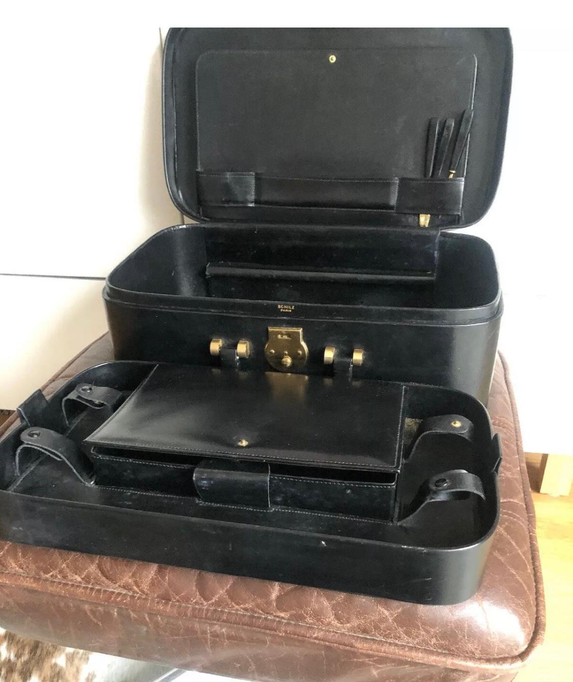 A 20th century French vintage collectible beauty case in black leather and gold details by Schilz Paris (signed). It has two compartments with the top one being removable. There are four leather straps with press buttons probably for watched or