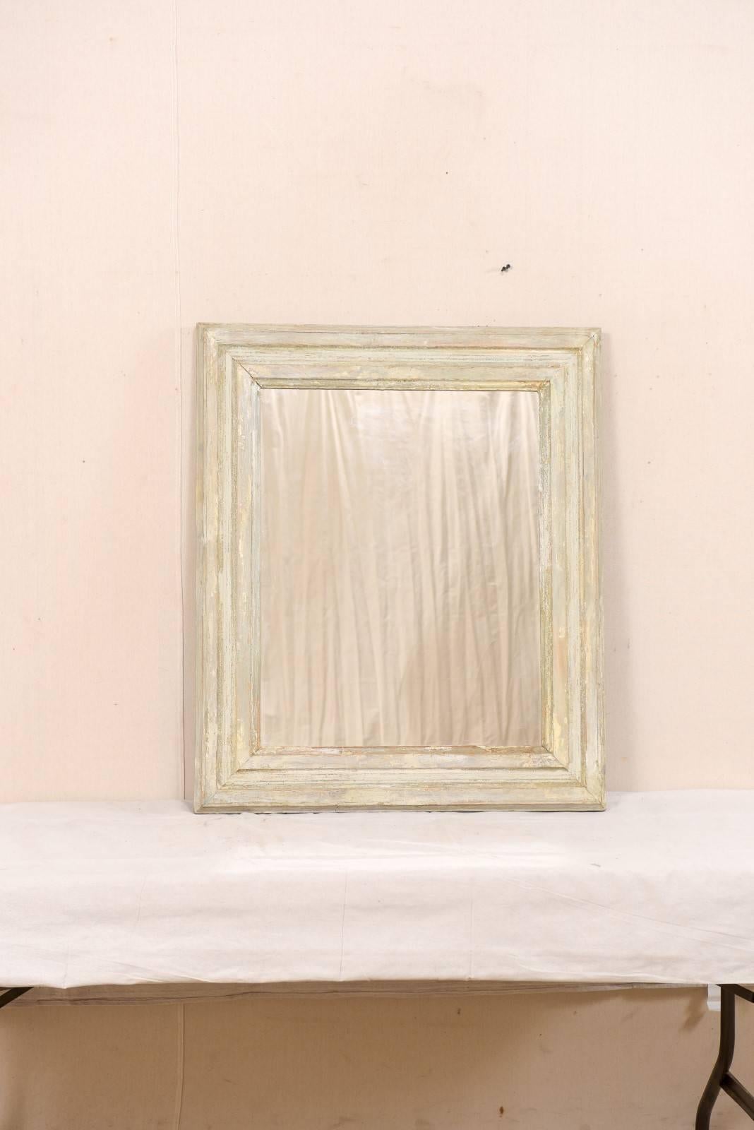 A vintage French painted wood mirror. This French mirror, with it's simple and clean lines, has a heavily straight-lined, molded surround. The mirror has various grey tones and bone coloring, with wood grain showing through in several areas. This