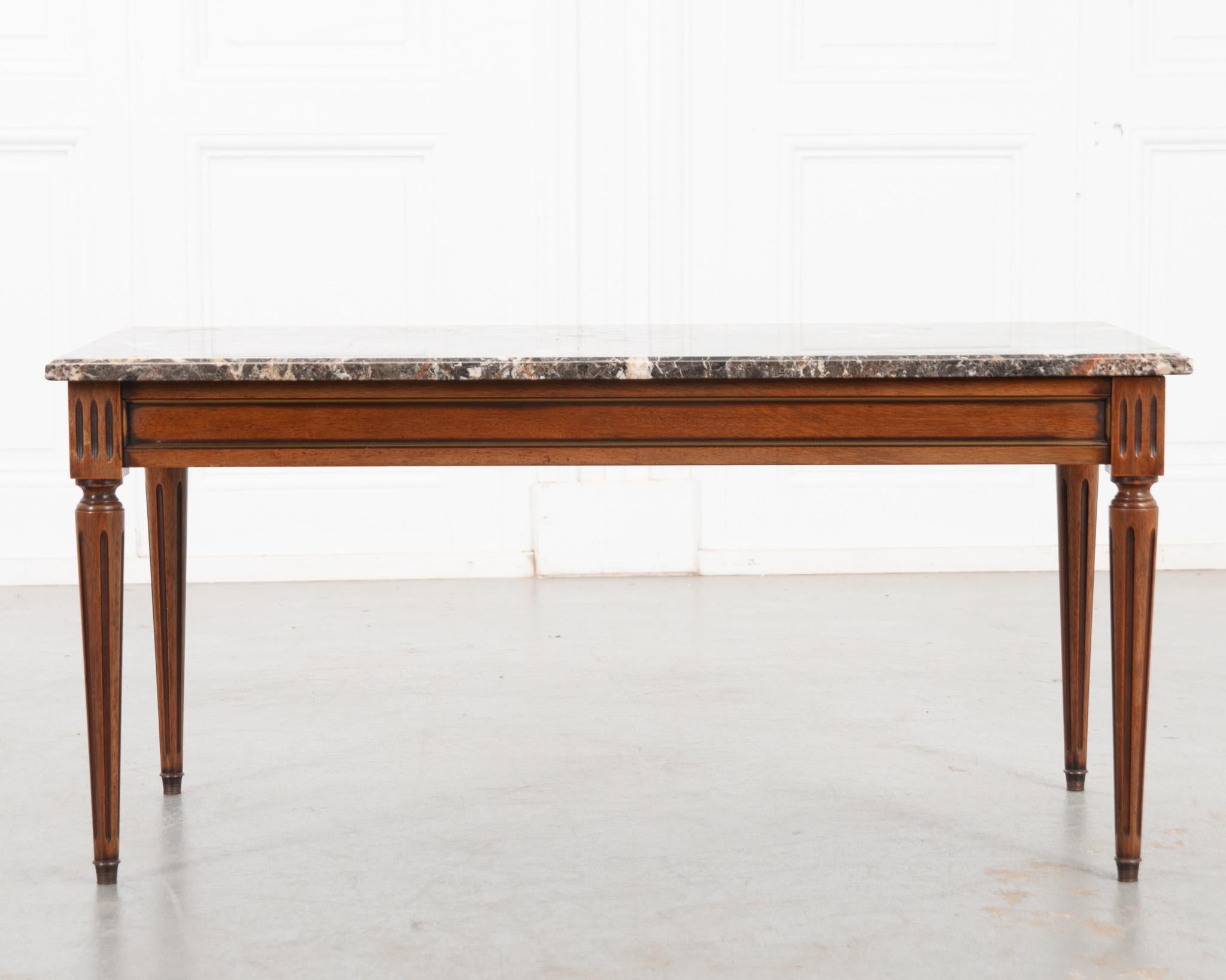 This vintage mahogany coffee table base is in the Louis XVI style and topped with an outstanding piece of colorful marble. It features a brass trimmed paneled apron with fluted, turned legs that taper to brass capped feet. A perfect low table ideal
