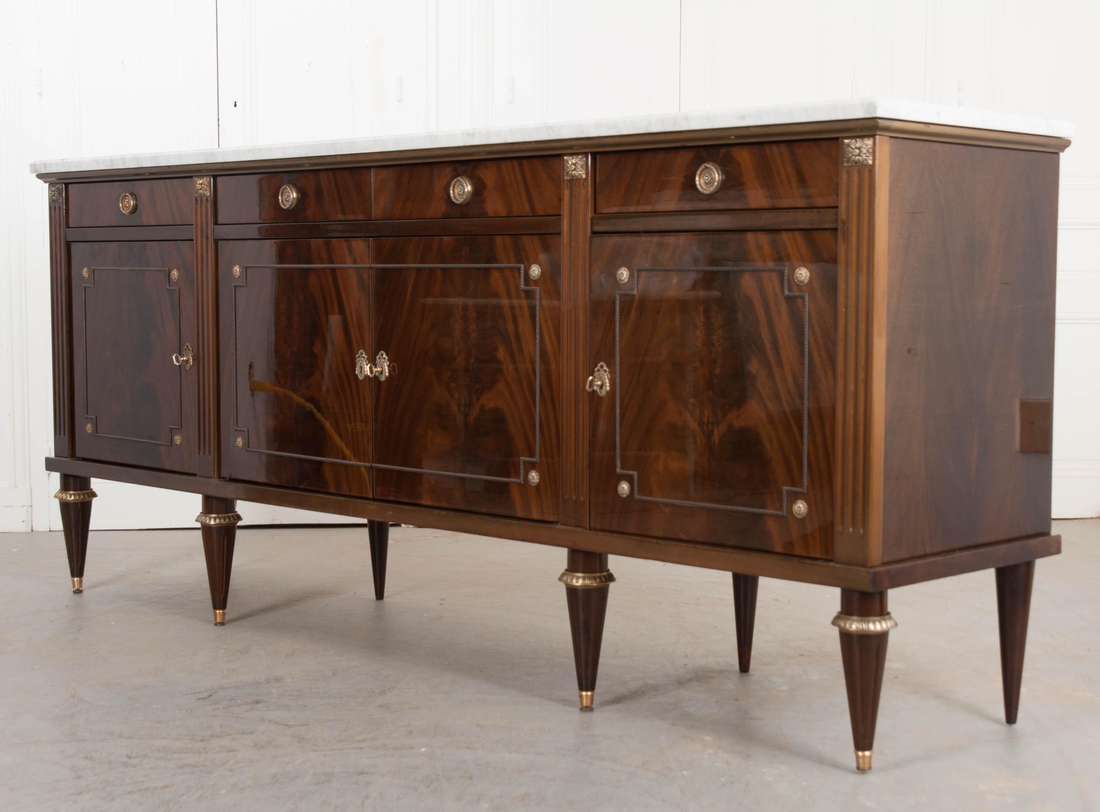This fine Louis XVI-style vintage marble-top enfilade, circa 1950s, was found in France and features a beautiful high-gloss lacquer which highlights the exquisite book-matched mahogany veneer. The carved white marble top with grey veining rests