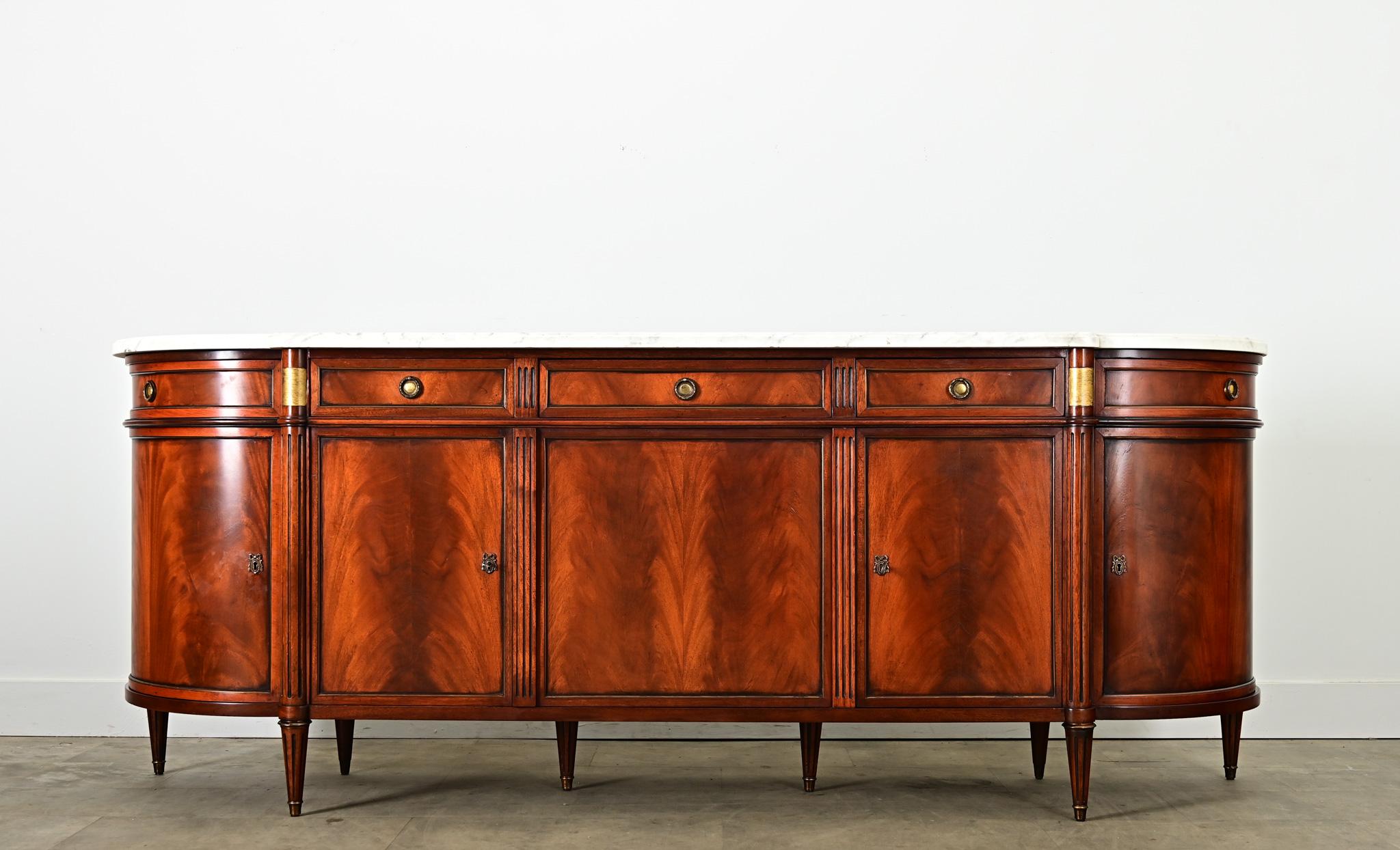 A statement piece for a dining room or foyer, this 20th century Louis XVI style enfilade speaks of refined taste and luxury. The white marble slab conforms to the breakfront of the demilune shape, protruding over the middle section before sloping