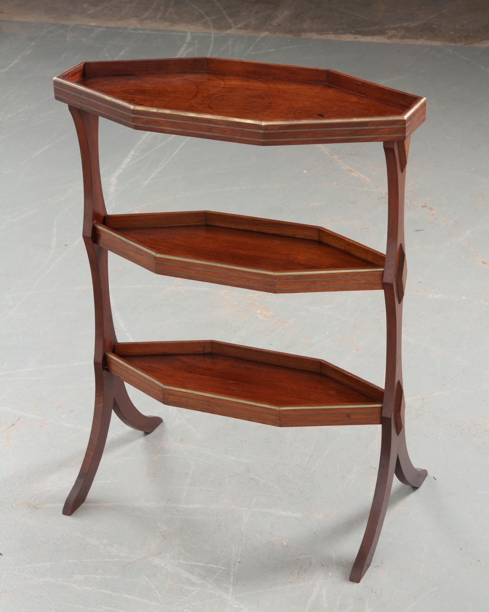 A petite vintage mahogany three tier table from 20th century France. The table features three shelves all inlay with brass bands; the elongated octagonal top with a larger raised rim and the lower two hexagonal shelves. Attractive raised diamond