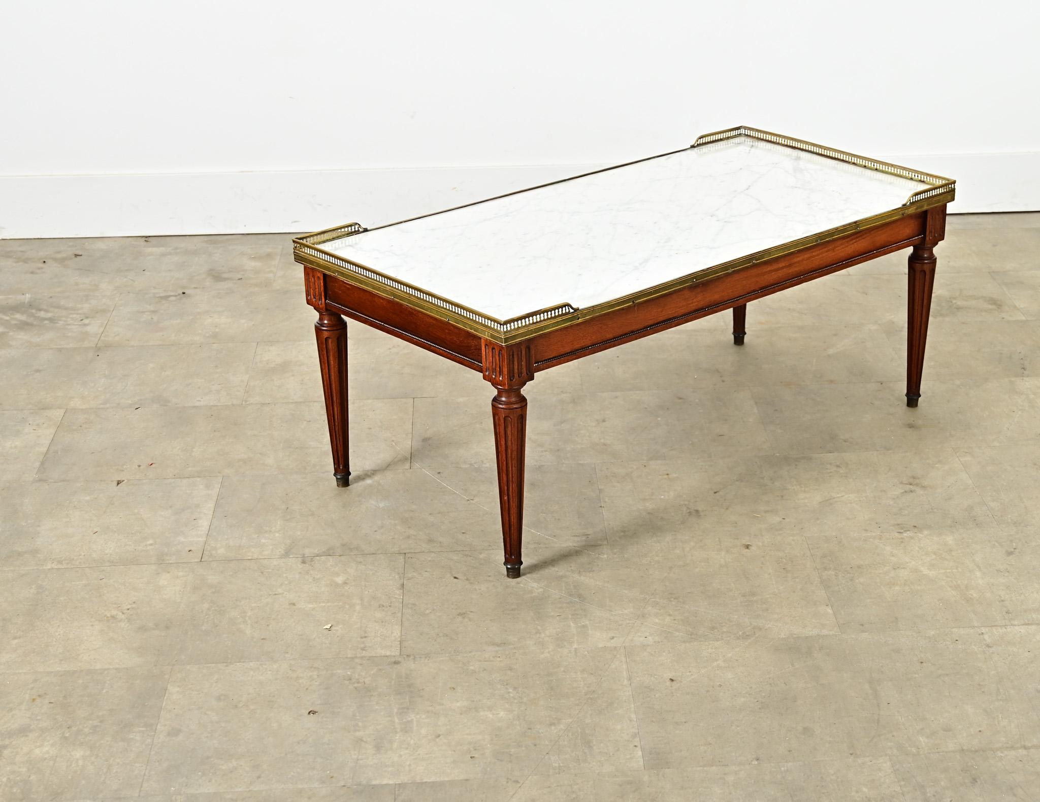 Like an iconic “Bouillotte” type table, this vintage (circa 1930) French Louis XVI inspired rectangular coffee or “low table” has all the signature elements of earlier design periods. The inset white marble top is surrounded by a brass trim and