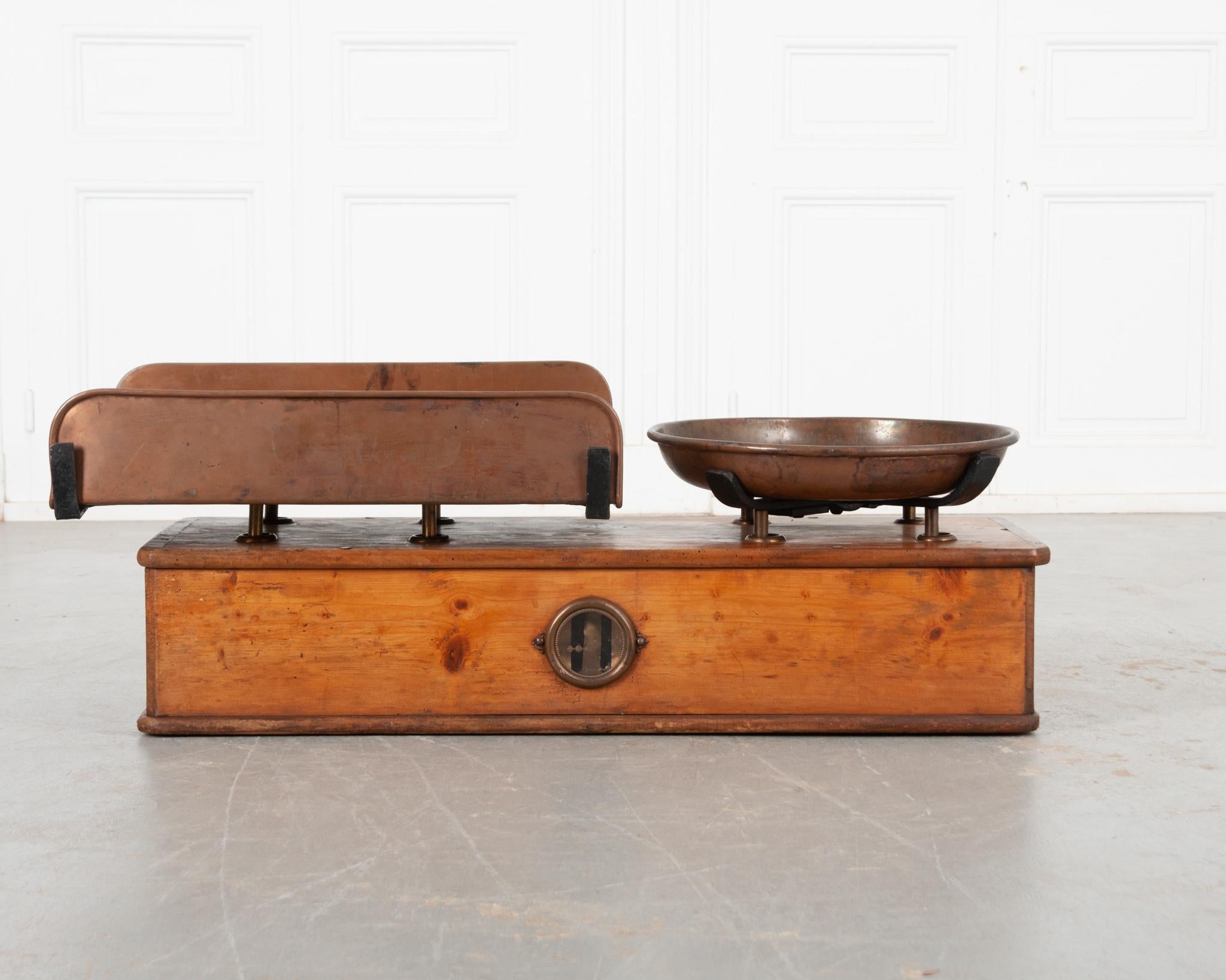 This massive culinary or produce scale from Lyon, France is the perfect antique accessory to elevate any kitchen. The base is made of solid waxed pine with a fantastic vibrant patina. Its sizable, heavy copper trays have aged wonderfully and bear
