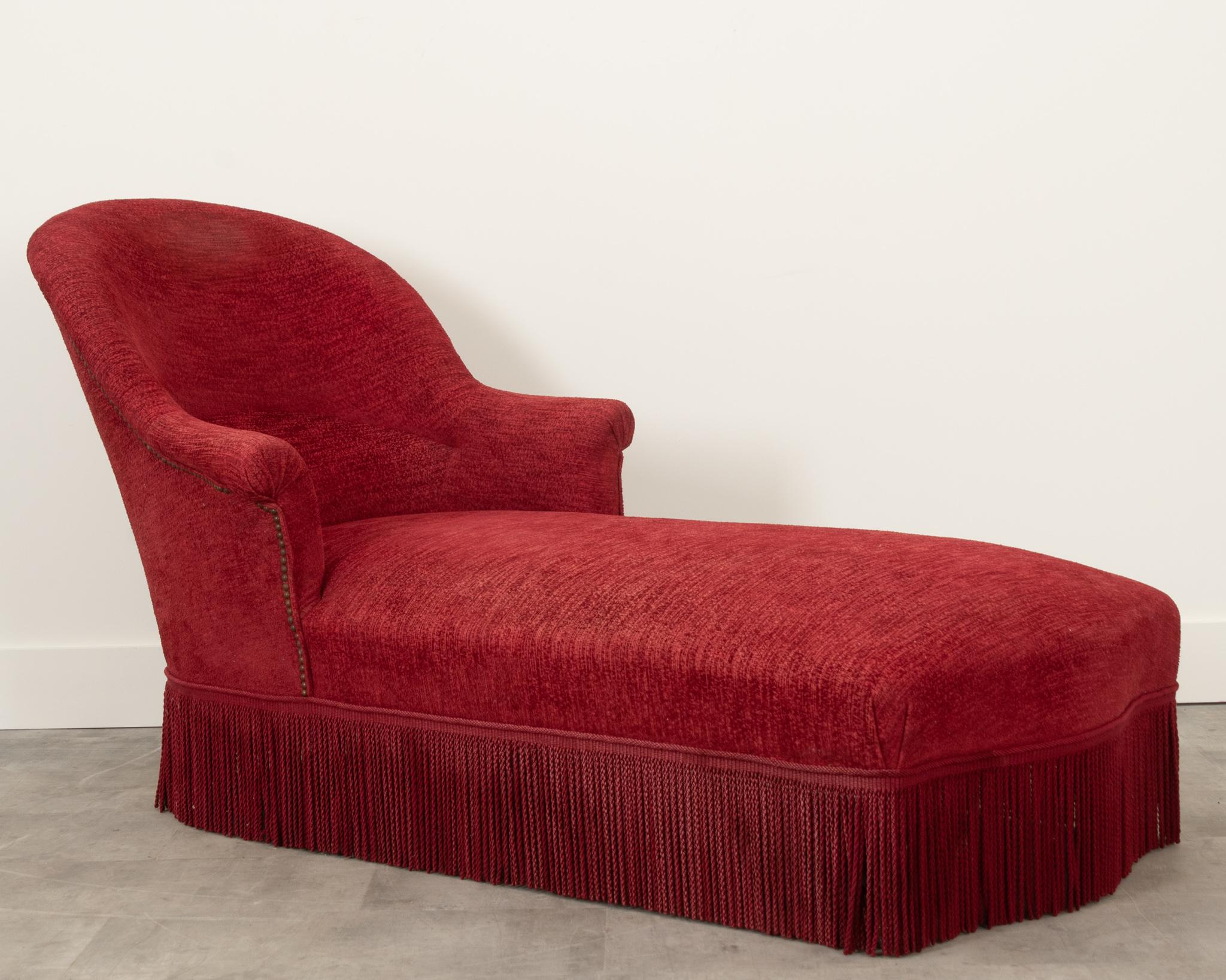 A beautiful eye-catching red textured velvet chaise with a classic shape and fringe around the bottom to hide the turned wooden feet. The perfect combination of comfort and composition, this chaise would go perfectly in any living space. The