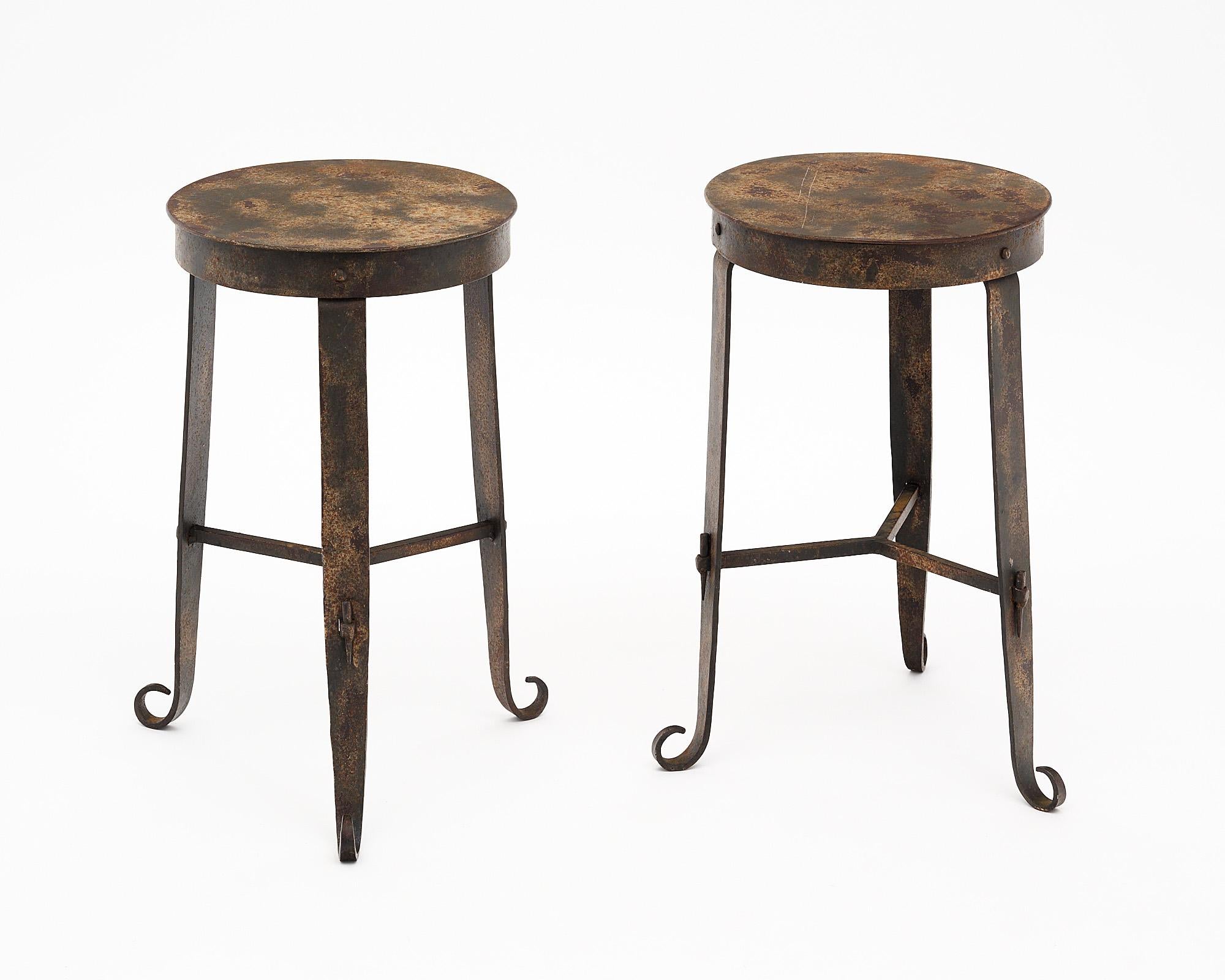 Vintage French side tables or stools made of metal. This pair has the original patina and curved feet at the base of the tripod structure. The diameter listed is for the widest point at the feet, the diameter of the top is 12”.
