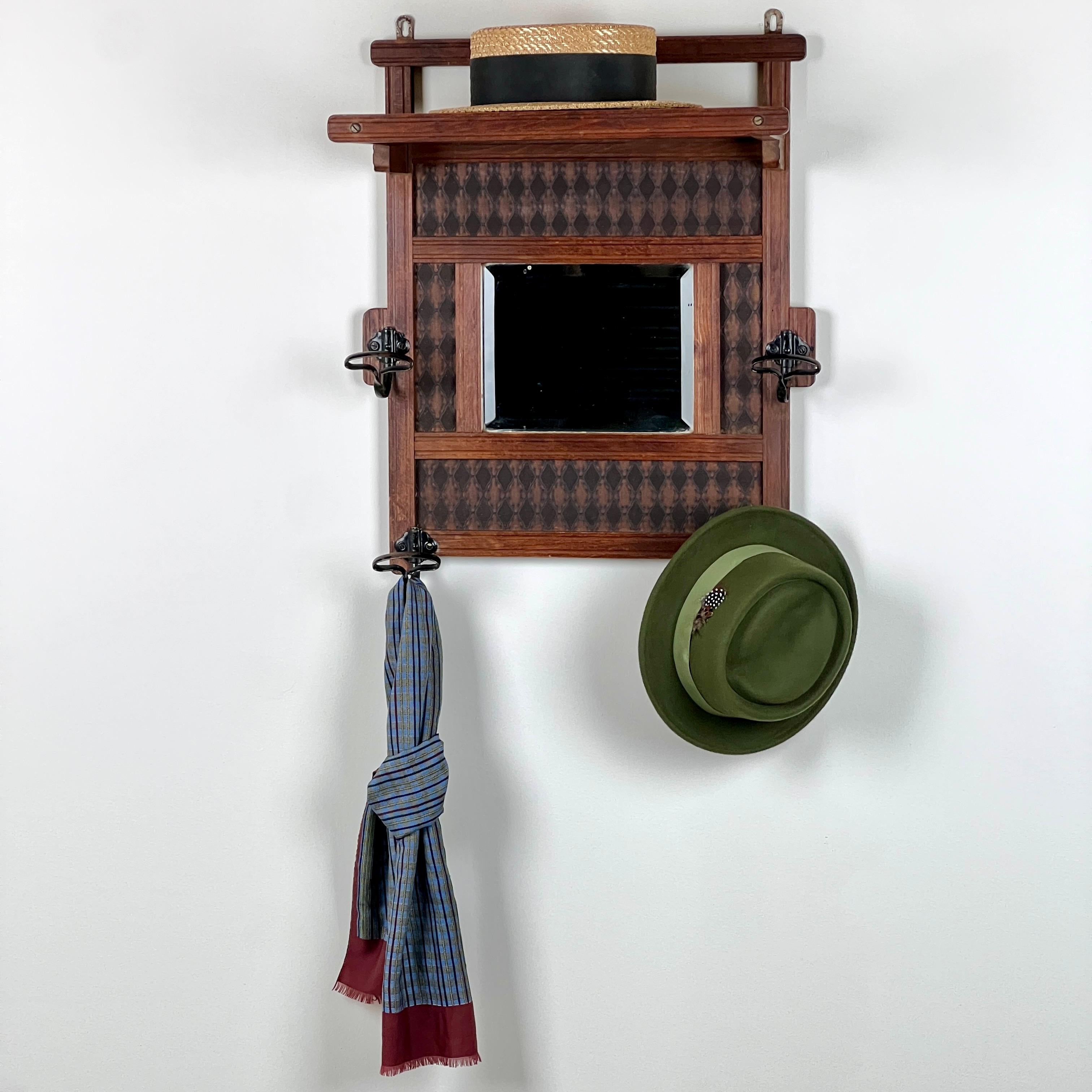Un grazioso appendiabiti francese vintage a specchio, composto da un ripiano superiore a doghe, ideale per cappelli, scatole, etc. In basso, la piastra centrale a specchio smussato è affiancata da quattro ganci in metallo forgiato. La cornice in