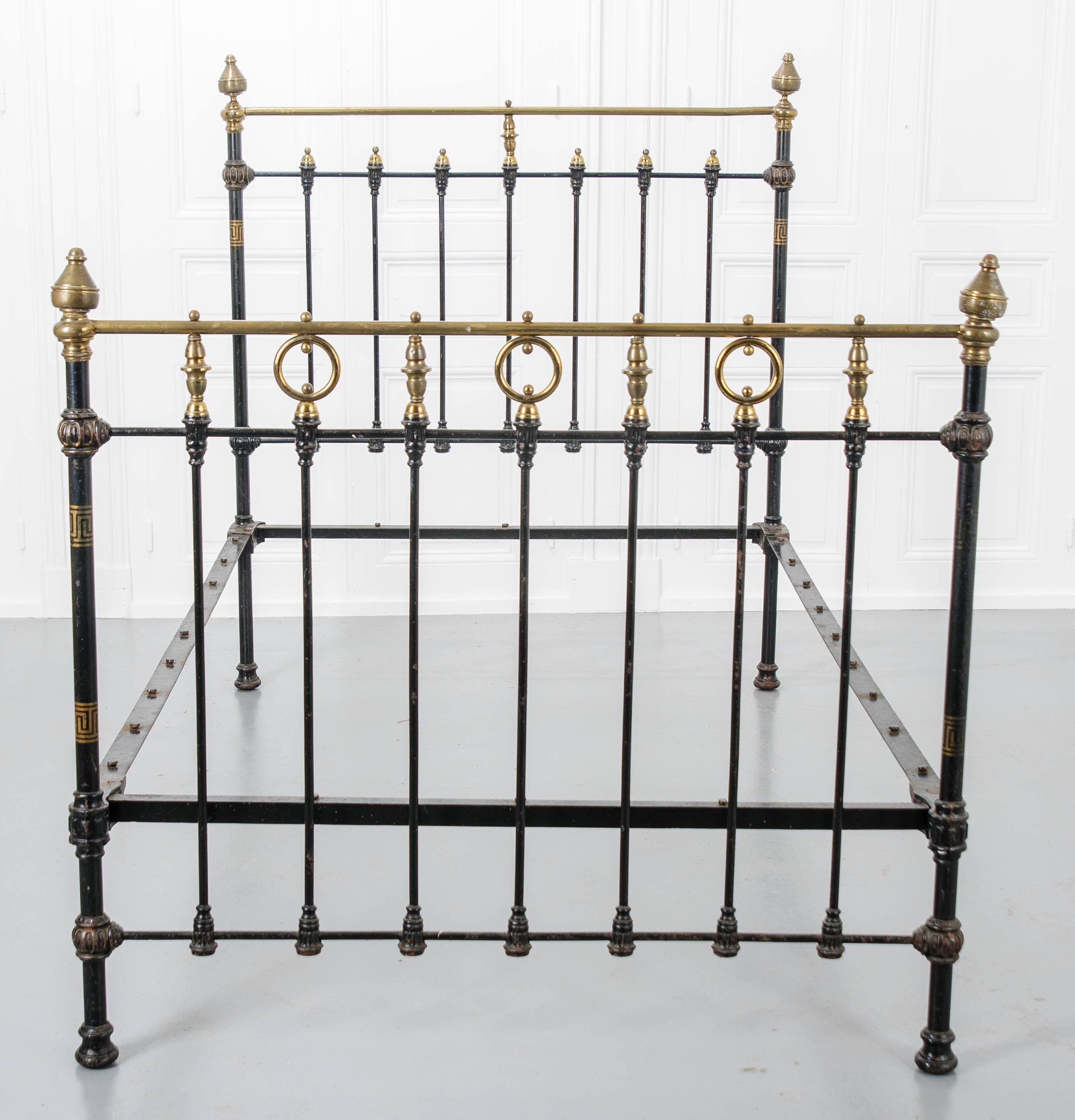 Brass finials adorn the four posts of this vintage French iron and brass full size bed. The cast iron frame has been painted black, which pairs with the metallic brass to create a smart and refined style. The frame features gold painted details,