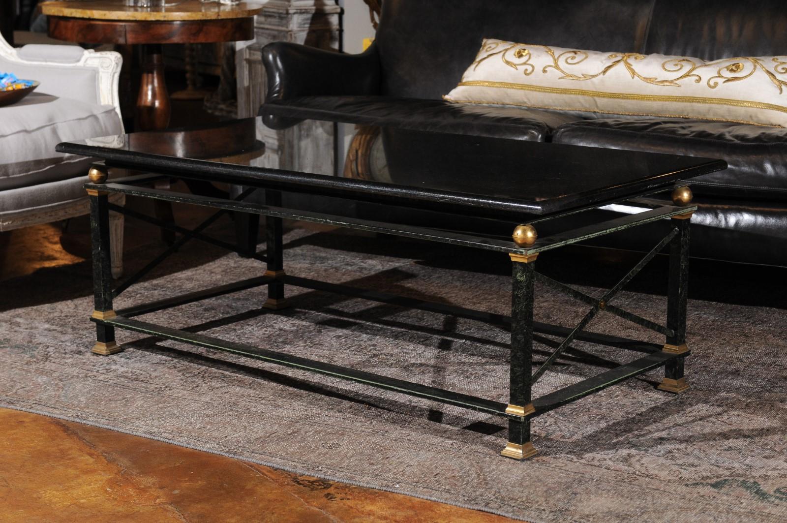 A French Parisian coffee table with black marble top and brass accents. This stylish French coffee table features a rectangular black marble top sitting above a linear iron base presenting a dark green undercoat. The straight legs, connected to one