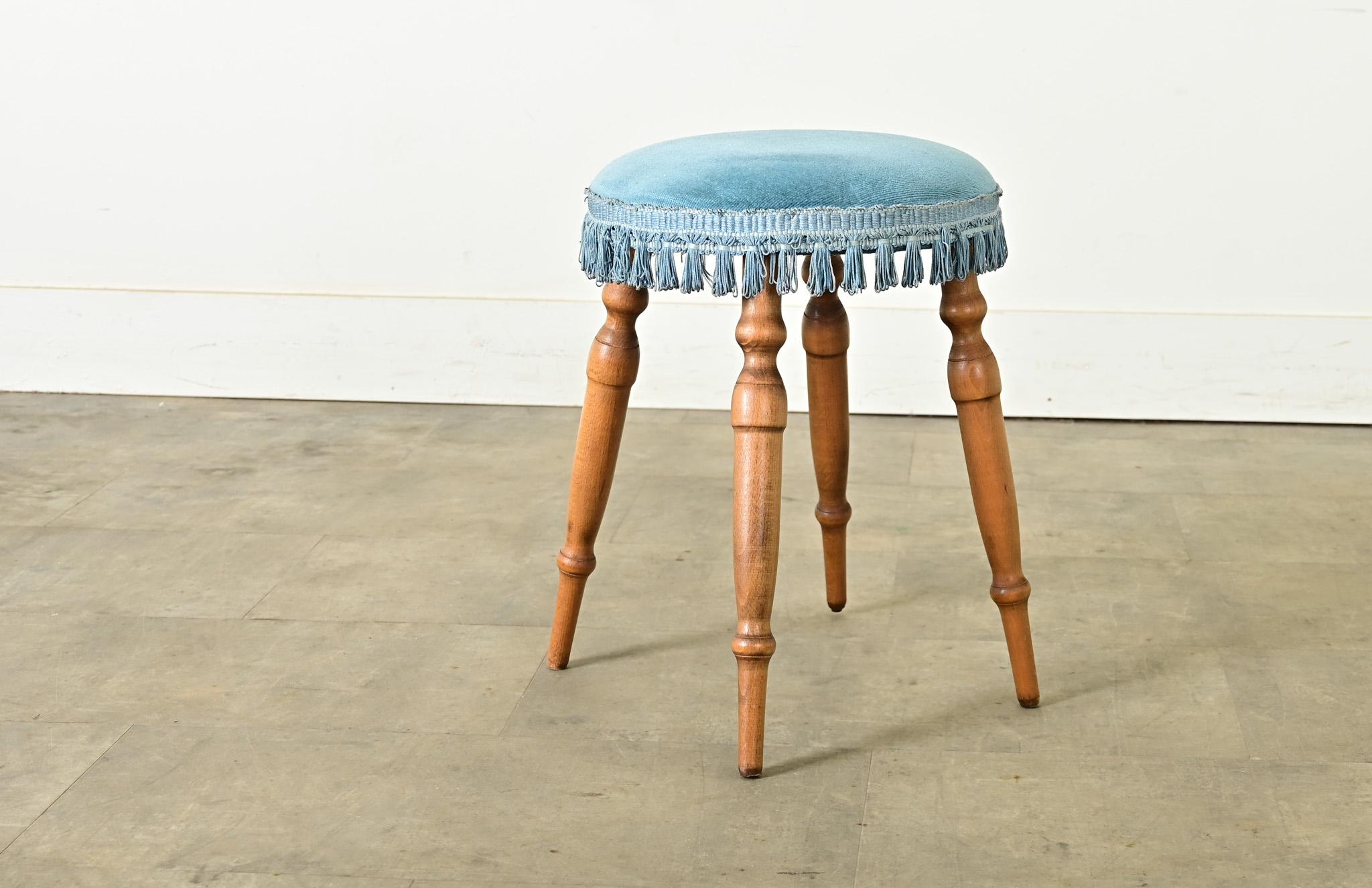 A charming little stool from France, vintage 20th century. Its simple and practical design is enhanced by an upholstered seat in blue velvet with short tassel trim, raised on four beautifully turned oak legs. This wonderfully patinated stool is both