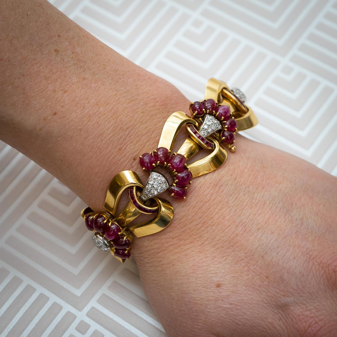 A French, vintage, ruby, diamond and gold bracelet, with six sets of pavé set round brilliant-cut diamonds, topped with five graduating cabochon rubies, with square, calibré-cut, channel set ruby curved bands, below the diamonds, alternating with