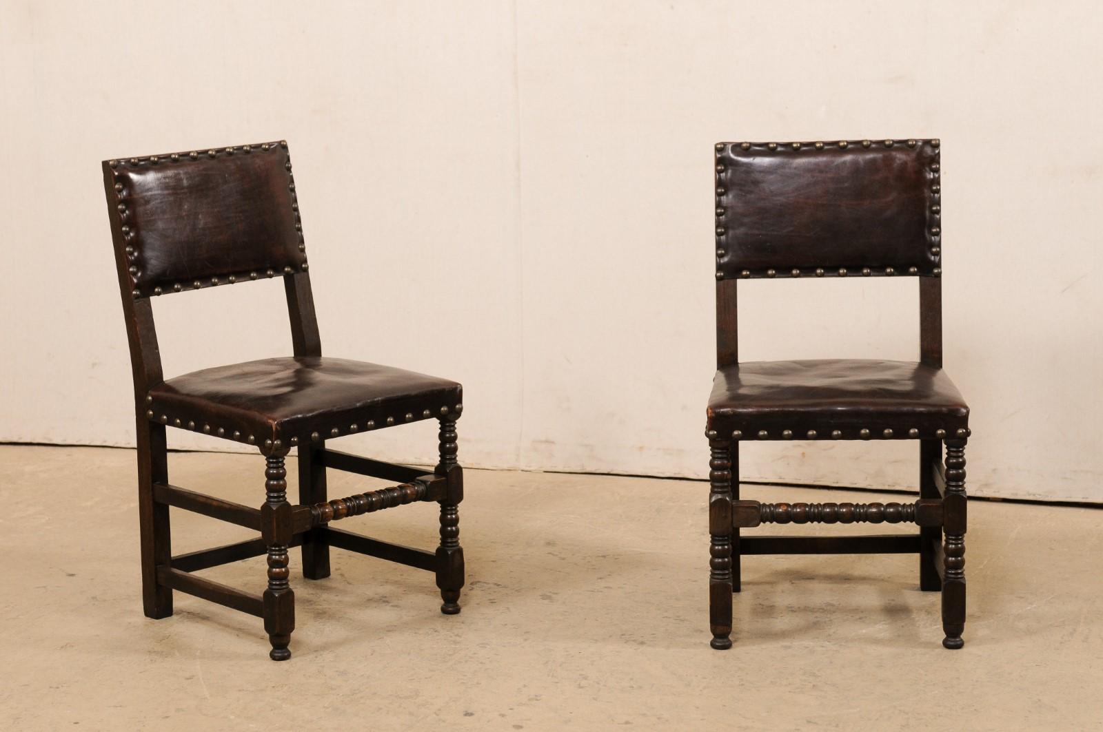 A French set of six carved-wood side chairs with leather seat and backs. These vintage chairs from France each feature their original leather upholstered back-rest and seat, with nail head trim adorning and outlining the perimeters, and presented
