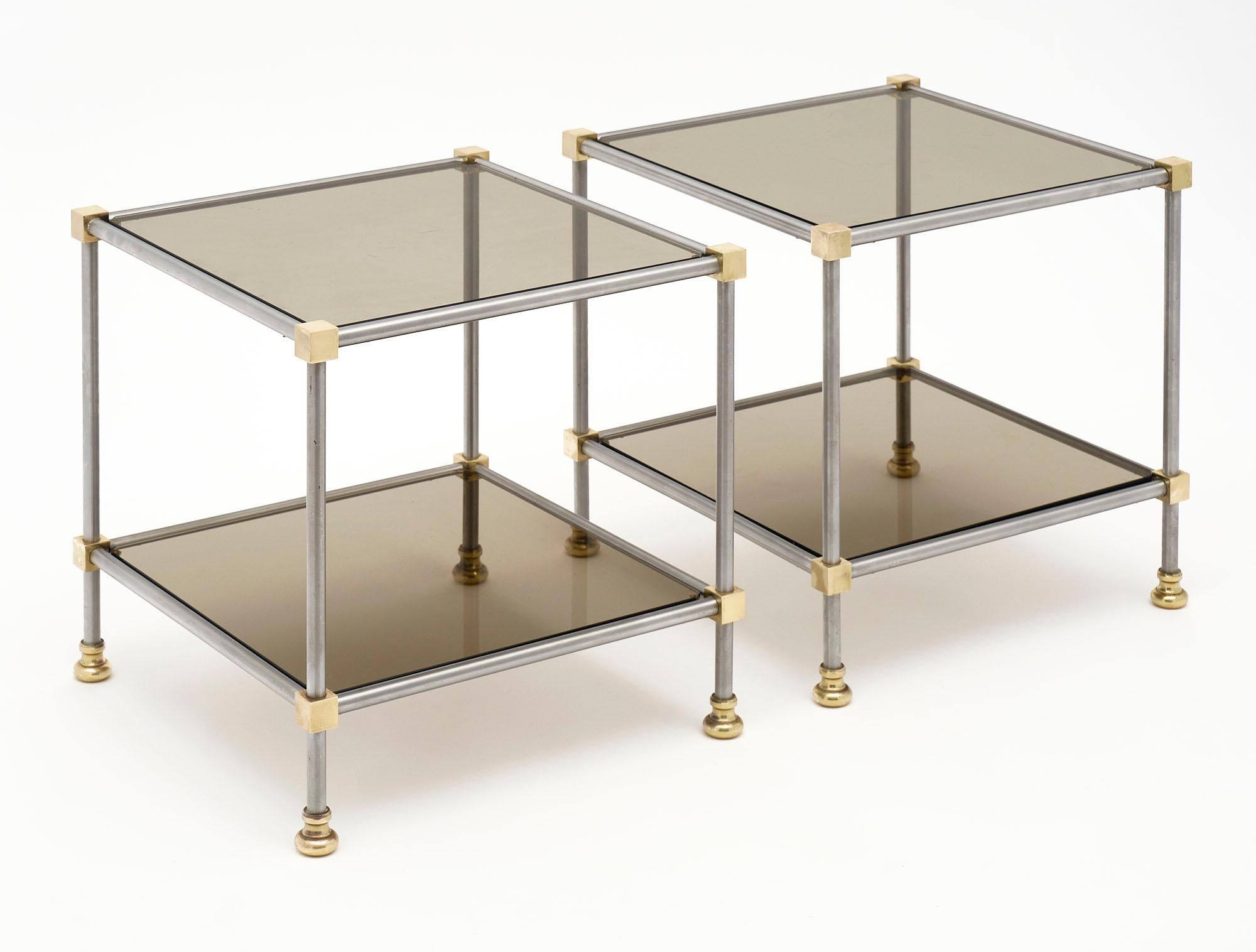 Pair of side tables from France made of steel and featuring brass cubic corners and brass feet. We love the smoked glass shelves and clean lines of this superb pair.