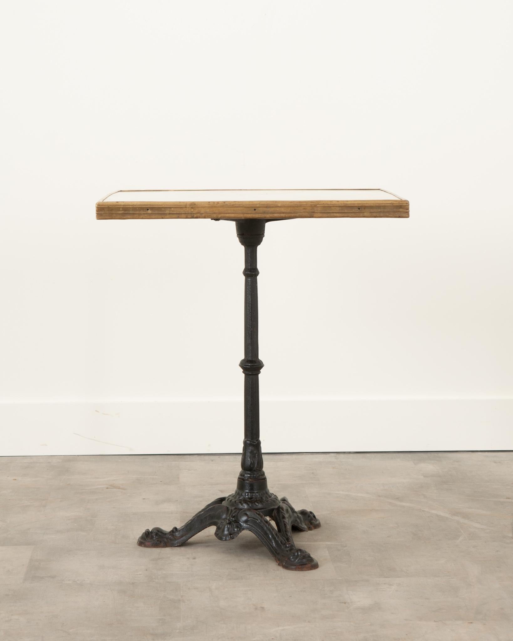 This sturdy bistro table is made from cast iron with a beautiful square formica top. The top is bordered by a brilliantly- patinated wide brass band and affixed to a cast iron tripodal base. There are some visible scratches on the top, adding to the