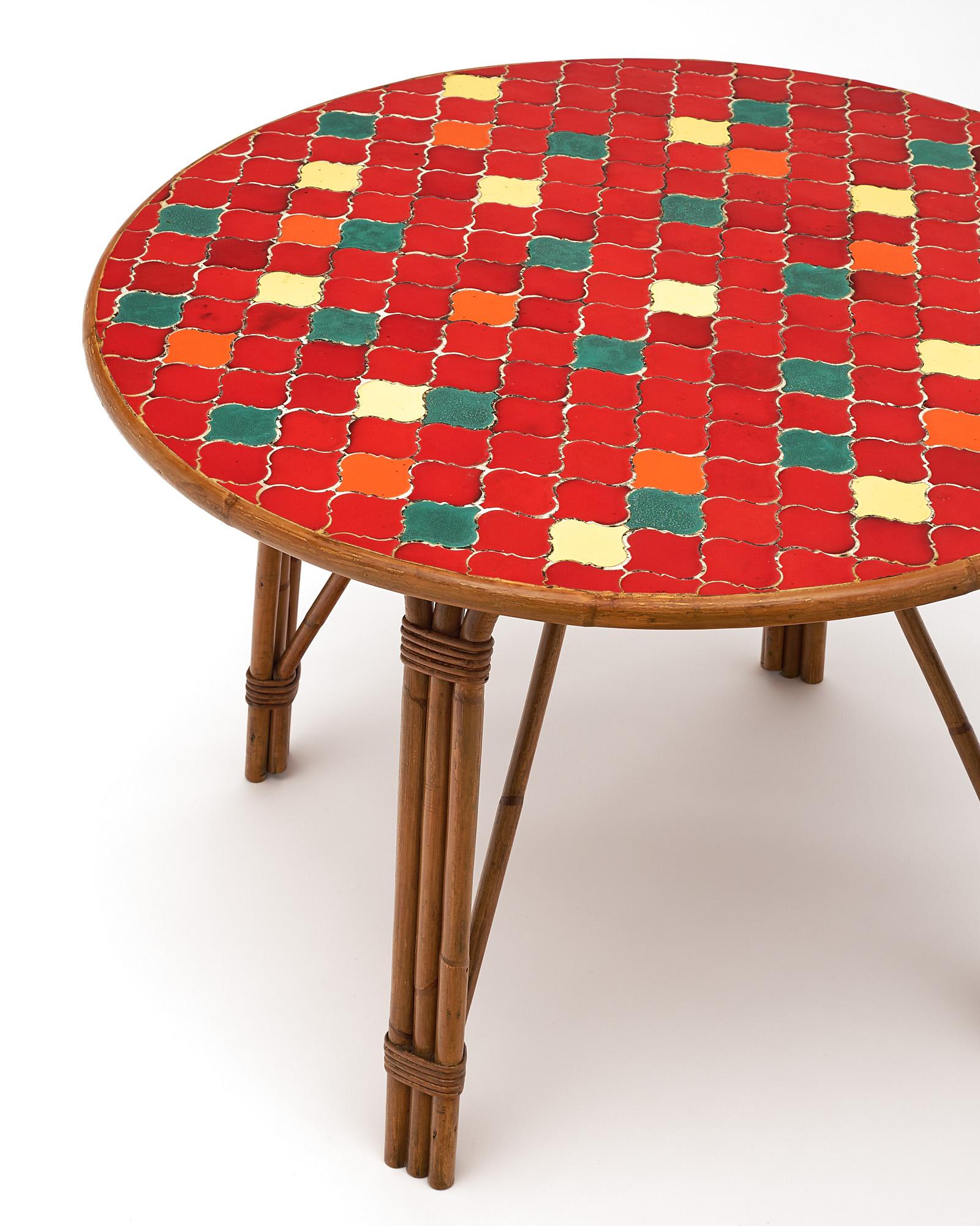 French table with bamboo legs supporting a tiled top in the manner of Audoux Minet. This piece features brightly colored red, yellow, orange, and green ceramic tiles. We love the unique style and energy it brings to a space!
