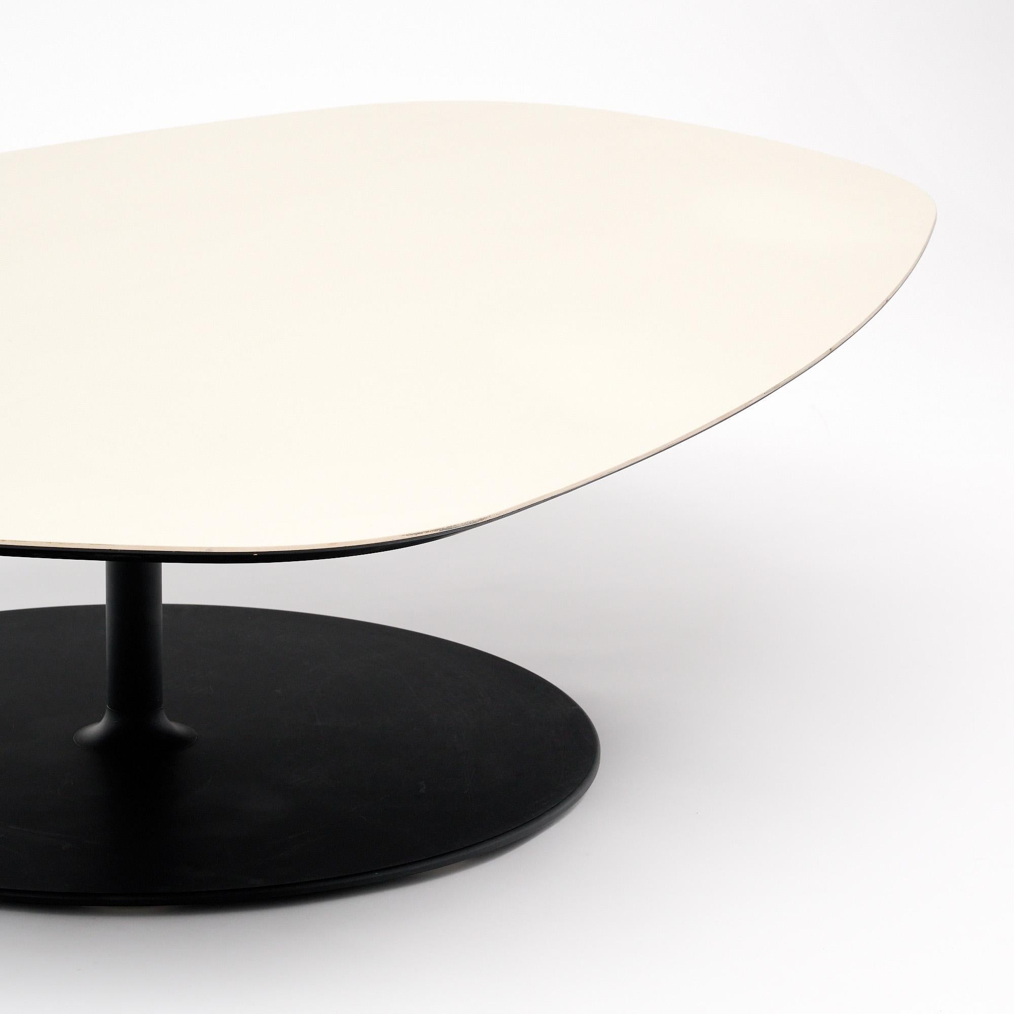 Table basse de France avec un plateau de forme unique et a-symétrique. La surface de cette pièce est recouverte d'un placage blanc vinylique. La base est une base métallique en forme de tulipe avec une finition noire. La pièce est en très bon état