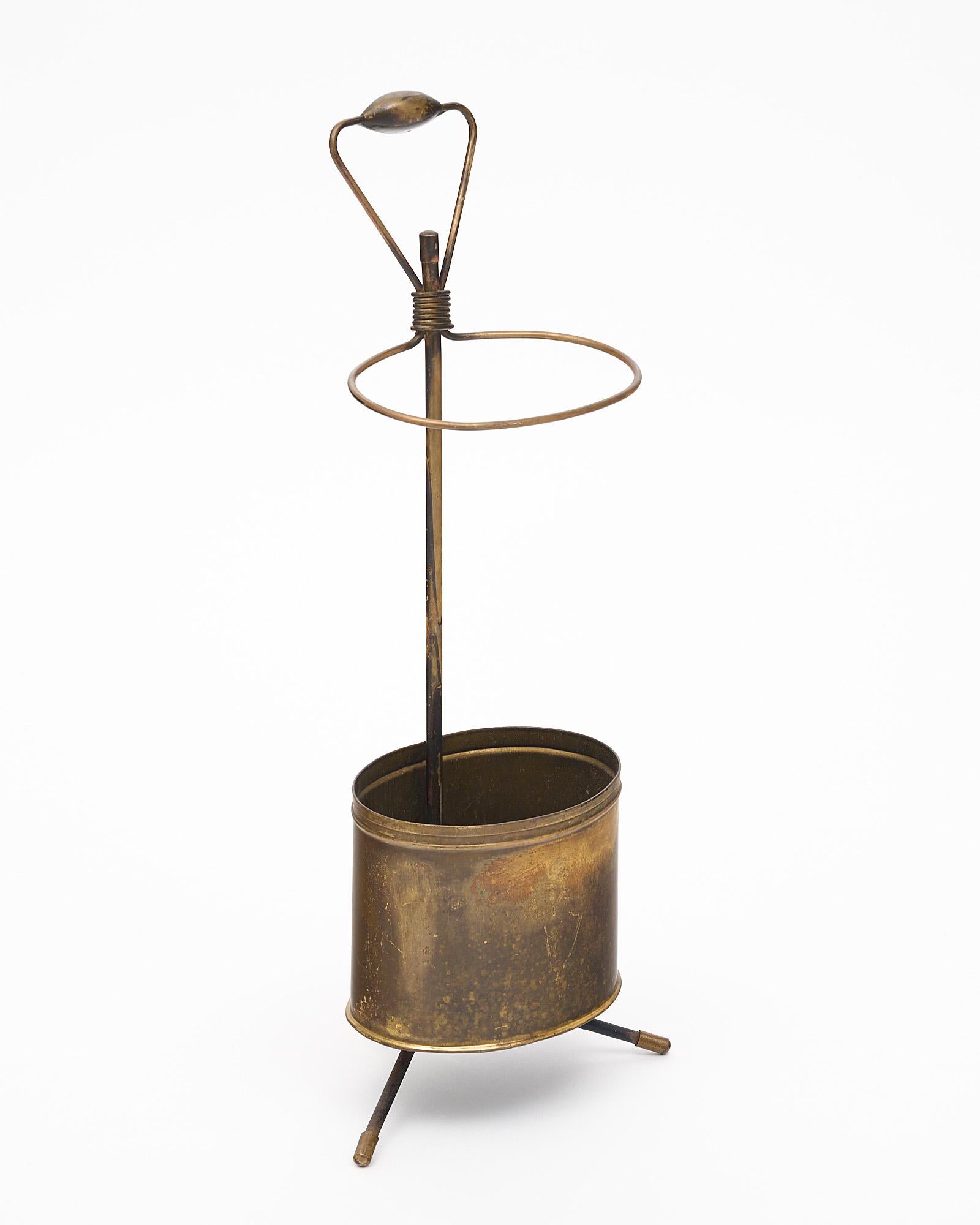 Umbrella stand made of brass from France in the manner of Jacques Adnet. This piece sits on a tripod base and has a functional holder at the base. There is a handle and a top holder.