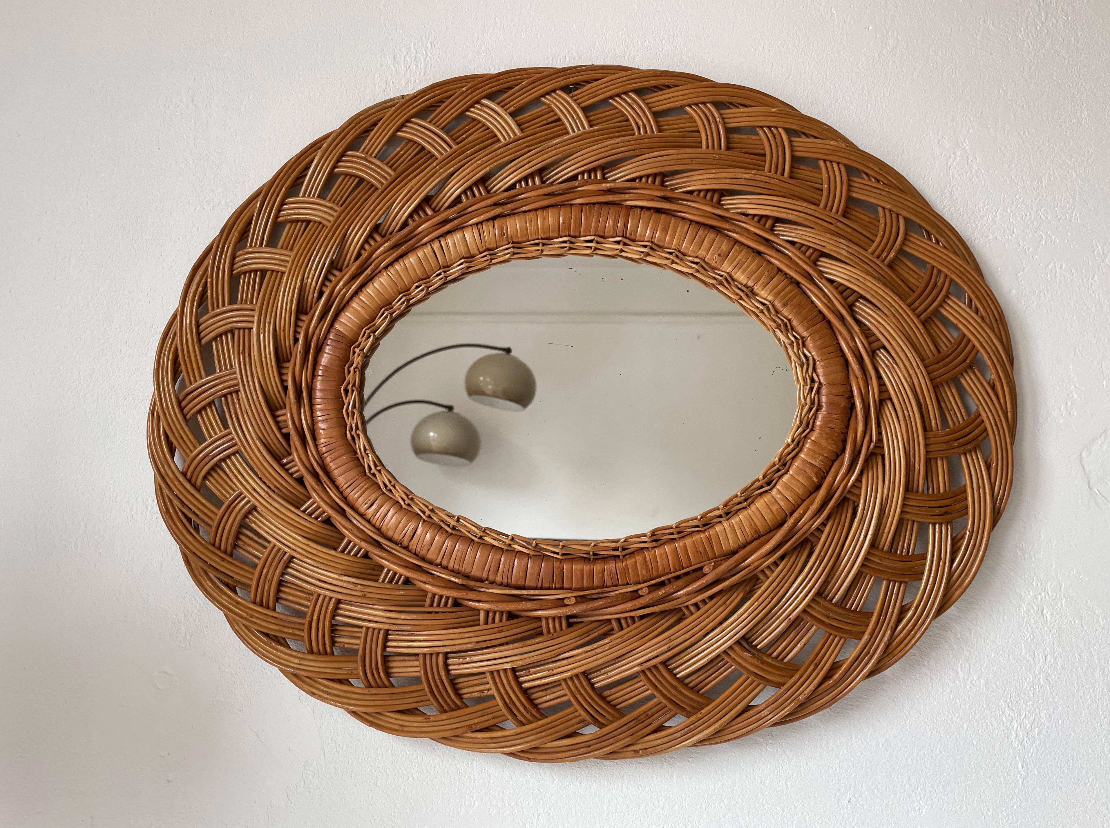 French Riviera 1950s oval hand woven and braided rattan mirror. Large wicker decorated frame with soft organic shapes that allows for hanging the mirror vertically or horisontally to add to a Bohemian Mediterranean style. Beautiful vintage