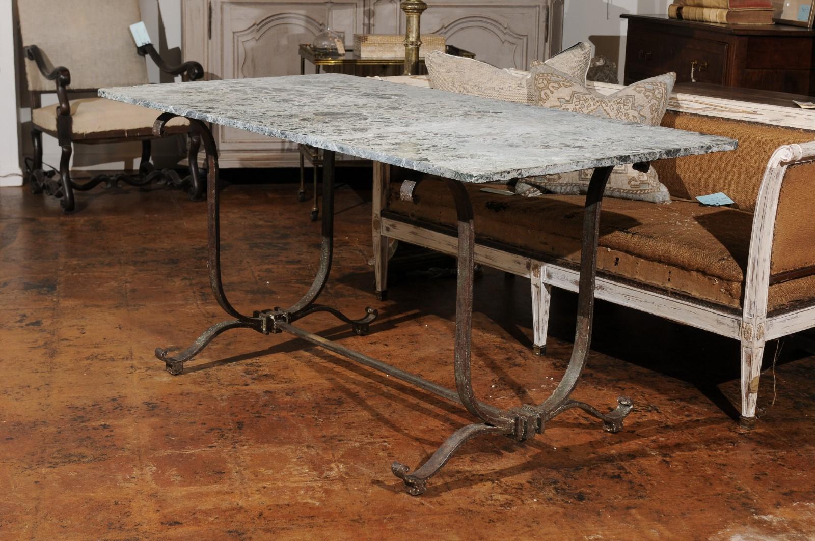A vintage French wrought-iron garden table from the first half of the 20th century, with its original marble top. This French garden table features a rectangular marble top with rounded corners, sitting above an interesting wrought-iron base. The