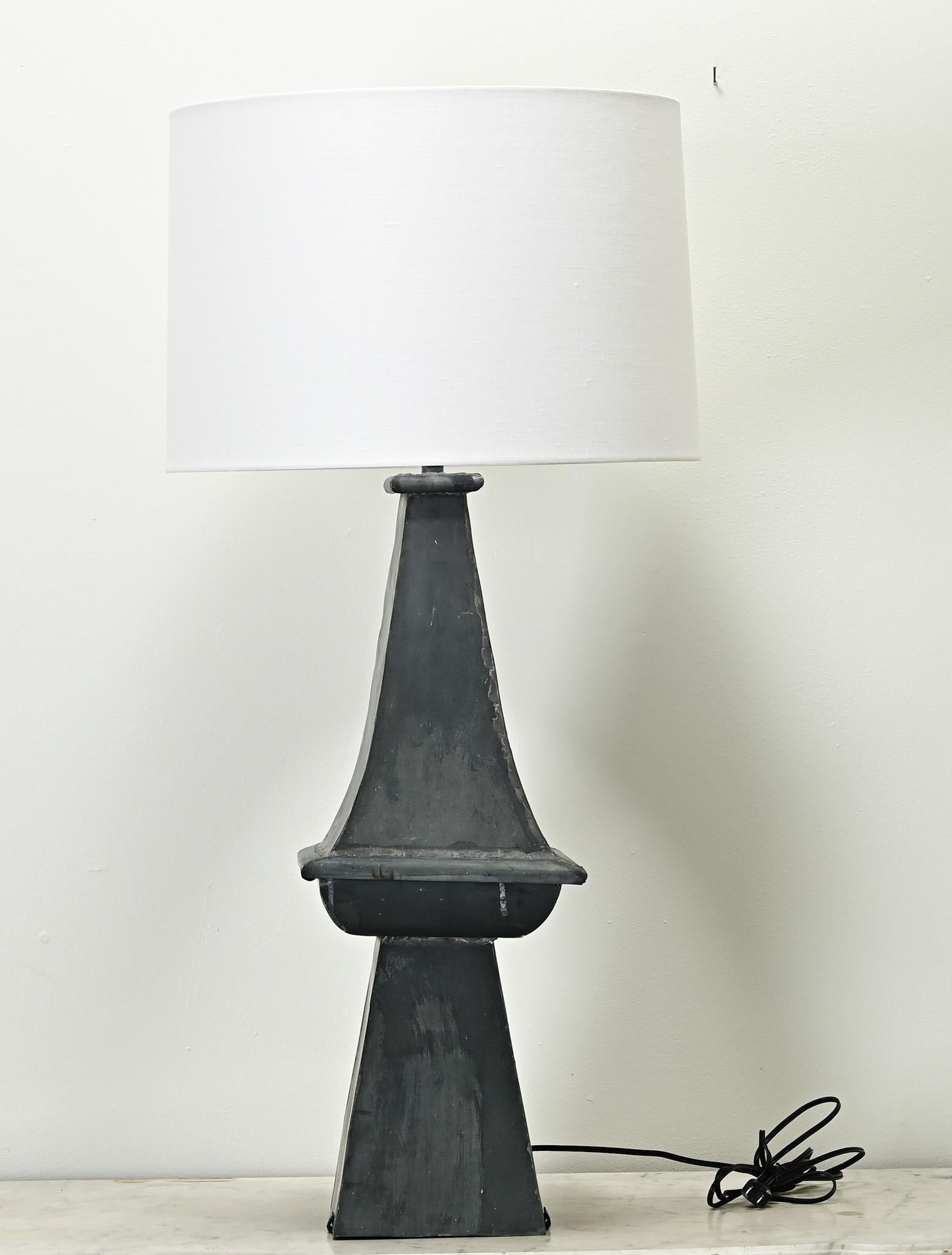 A tall vintage zinc table lamp made in France with a new linen shade. Once an architectural element, this lamp is made from a rooftop finial and has a beautiful patina consistent with use. Professionally wired for the US using UL listed parts. Be