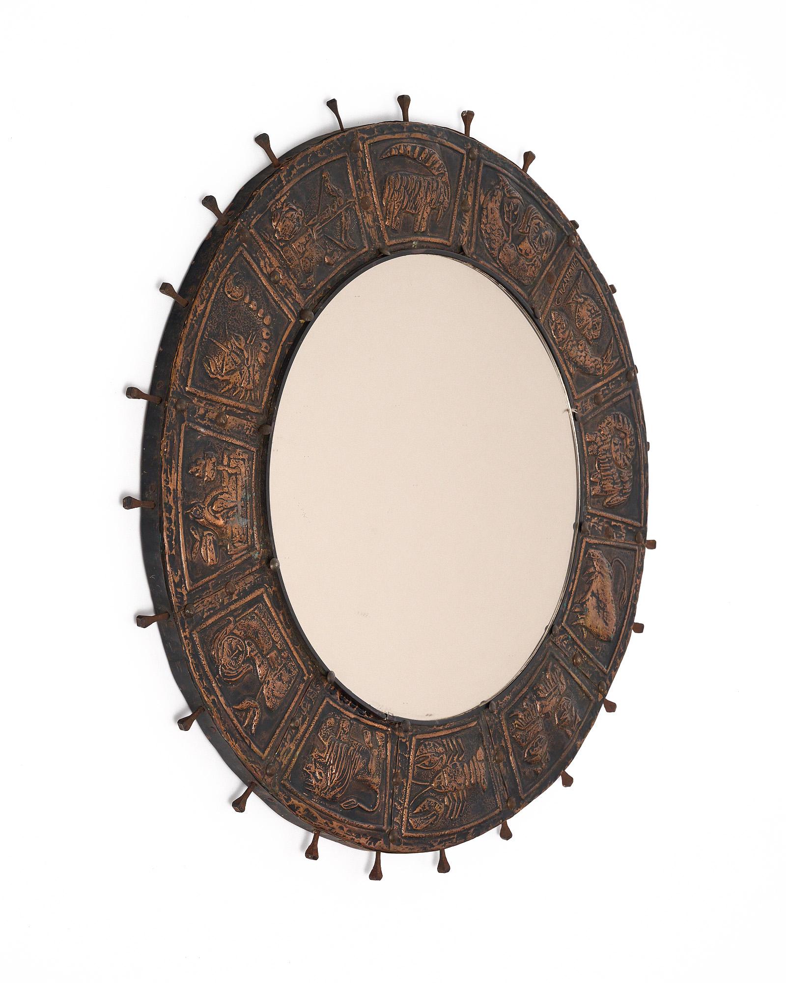 Mirror from mid-century France, featuring a circular frame of hand-hammered metal. The frame is adorned with designs showcasing the zodiac signs. The central mirror is circular as well.