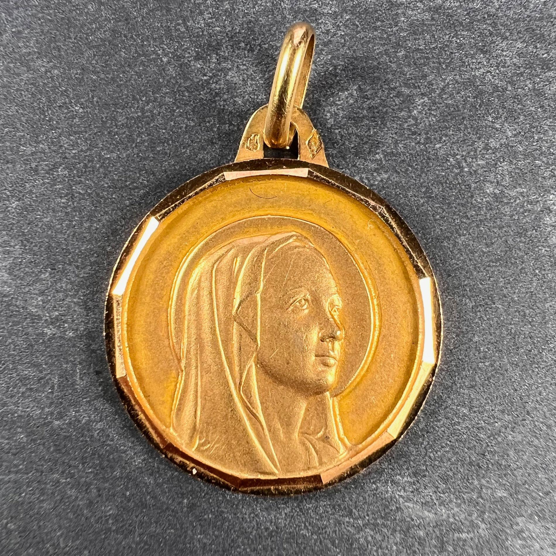 Un pendentif de charme français en or jaune 18 carats (18K) conçu comme une médaille représentant la Vierge Marie dans un cadre à facettes. Estampillée de la marque de l'aigle pour l'or 18 carats et de fabrication française avec une marque de