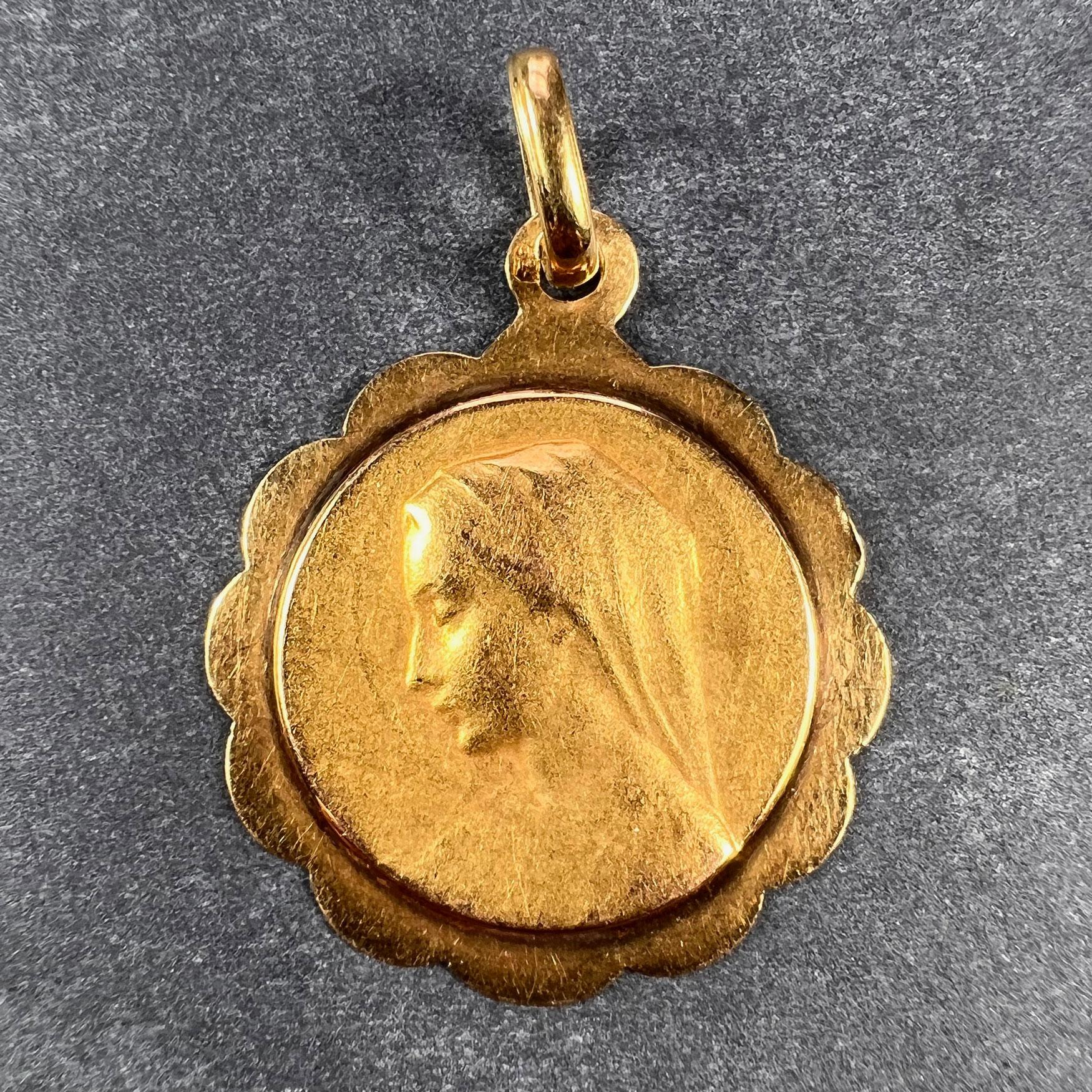 A French 18 karat (18K) yellow gold charm pendant designed as a medal depicting the Virgin Mary within a scalloped frame. Stamped with the horse’s head mark for 18 karat gold and French manufacture between 1838 and 1919, with an unknown maker's