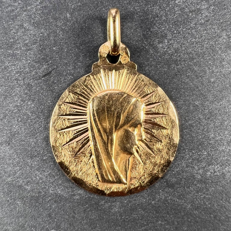 A French 18 karat (18K) yellow gold charm pendant designed as a medal depicting the Virgin Mary within an engraved sunburst. Stamped with the eagle mark for 18 karat gold and French manufacture with an unknown maker's mark.  

Dimensions: 2.2 x 1.8